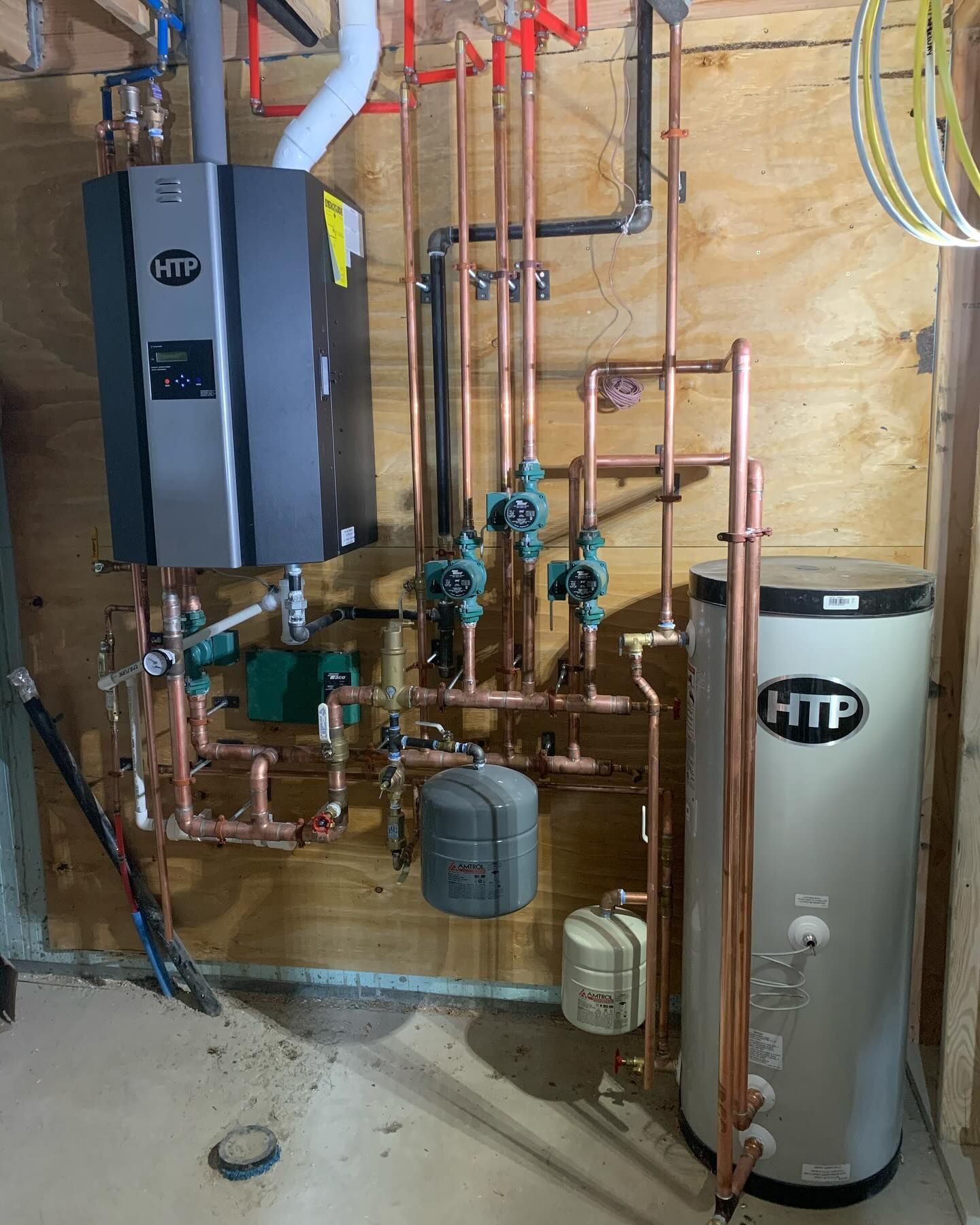 A wall-mounted HTP combi boiler connected to copper piping, circulation pumps, and an HTP hot water storage tank.
