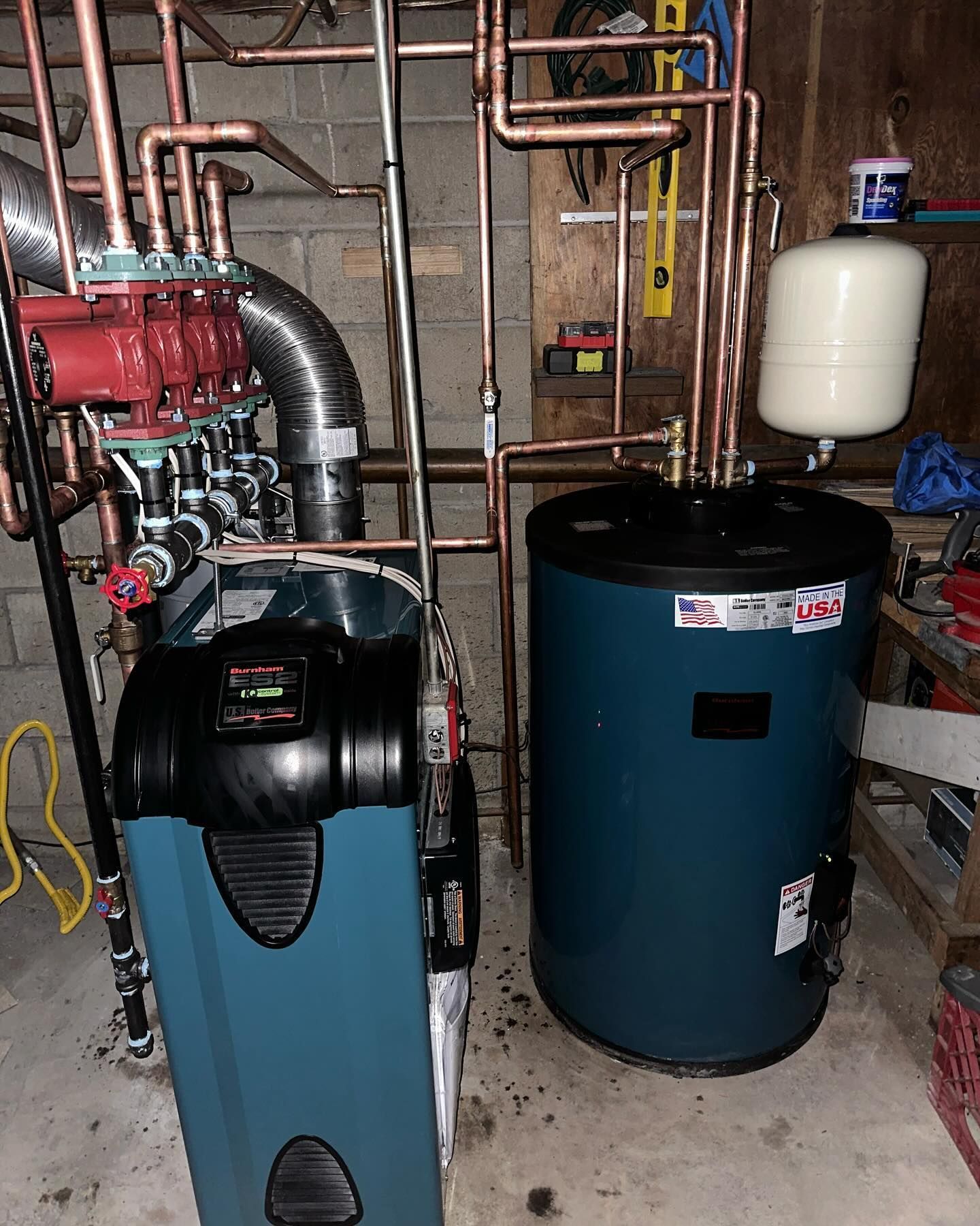 Residential heating system featuring a teal boiler, water heater tank, copper pipes, and circulator pumps in a basement.