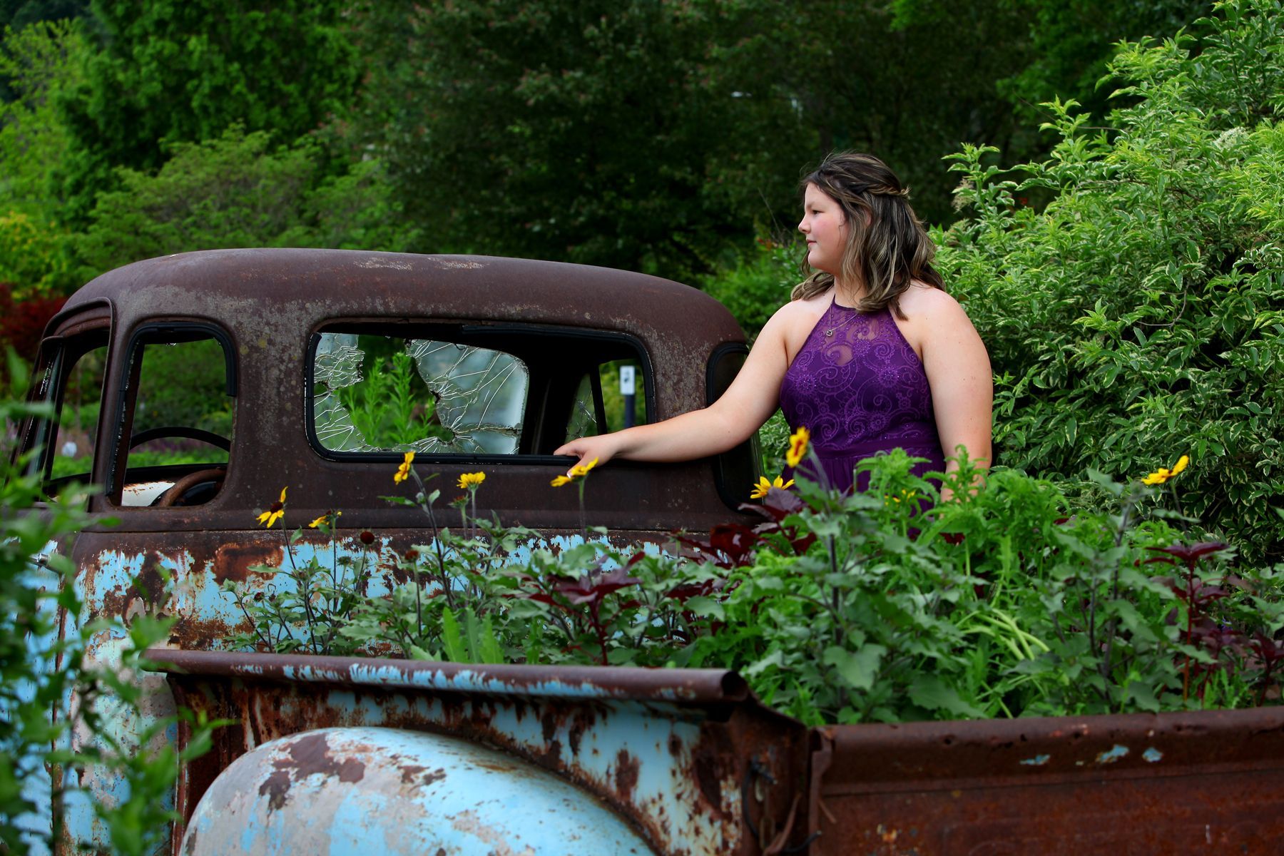 A woman in a purple dress is standing in the back of an old rusty truck.
