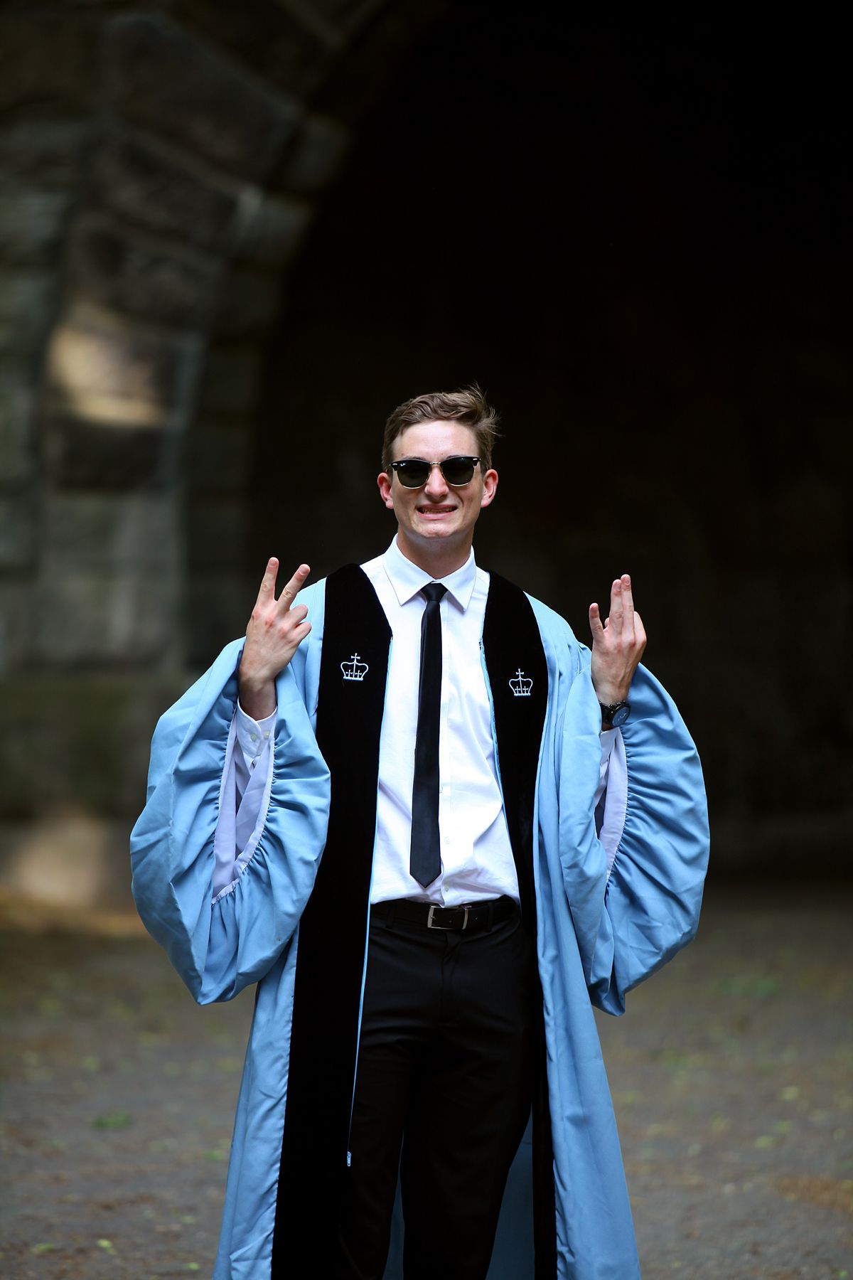 A man in a graduation gown and tie is giving the peace sign.