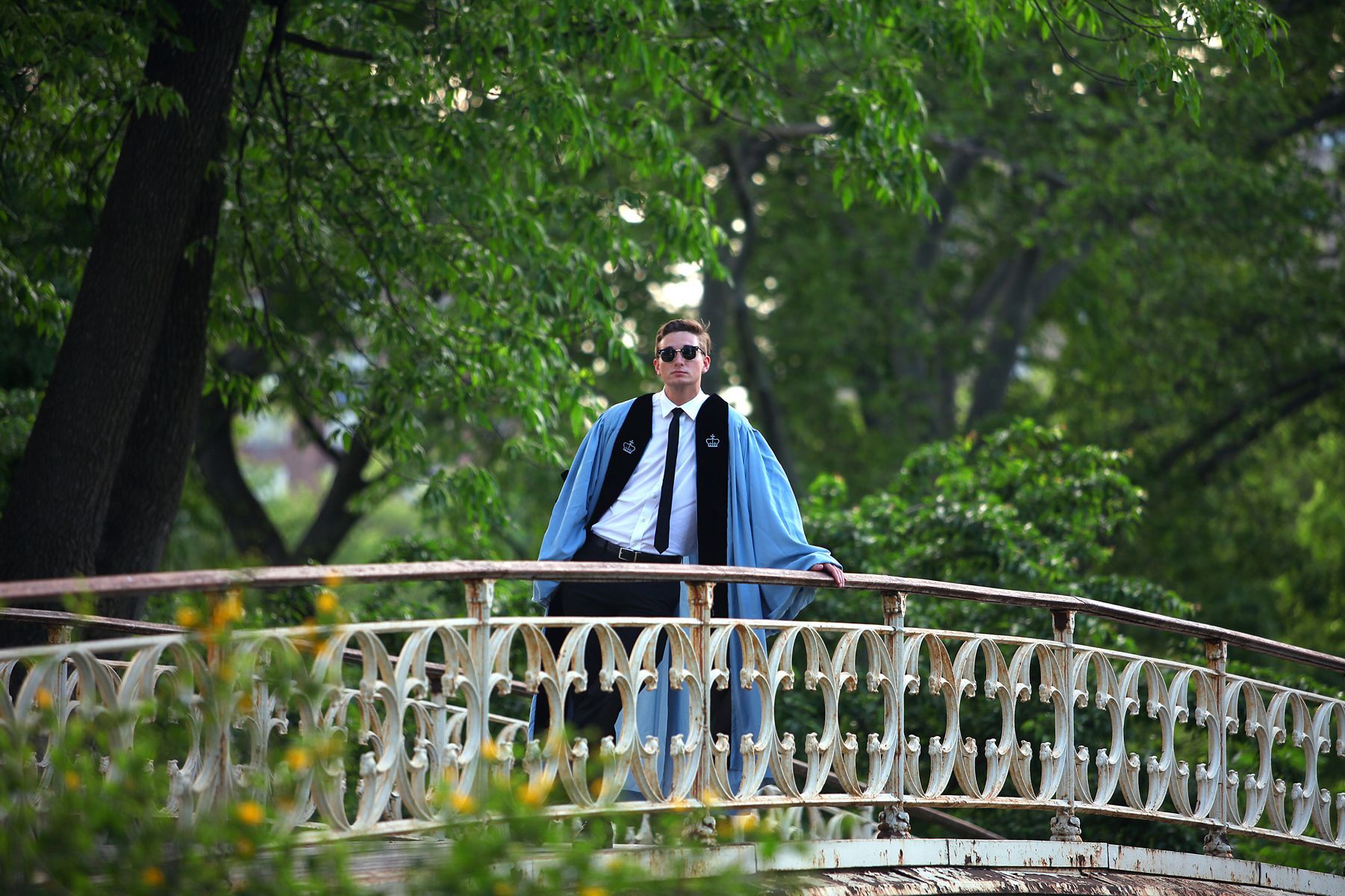 A man in a graduation cap and gown is standing on a bridge.