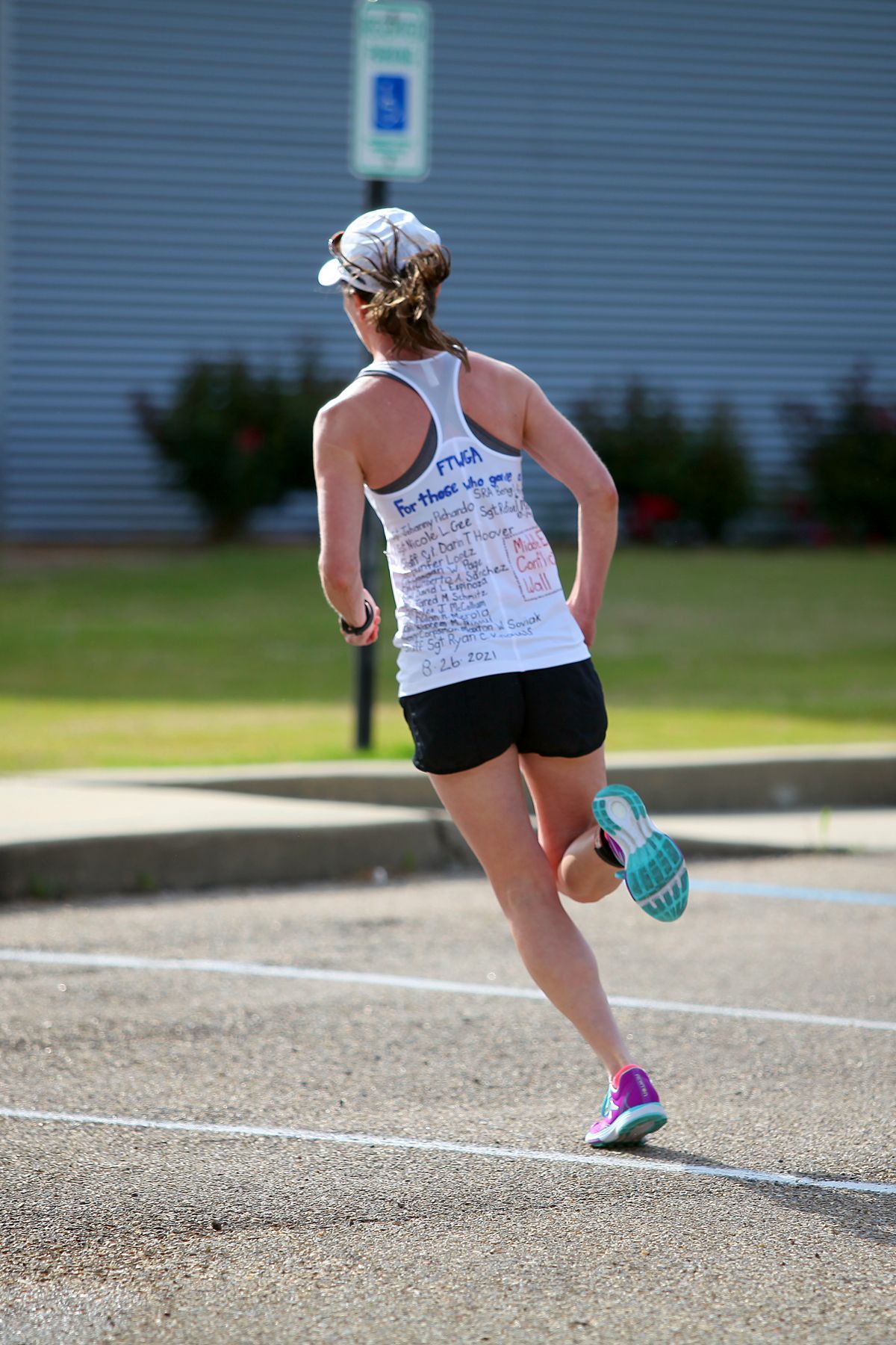 A woman in a white tank top and black shorts is running.