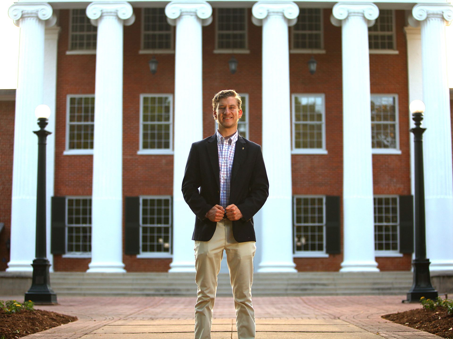 A man is standing in front of a large brick building with white columns.