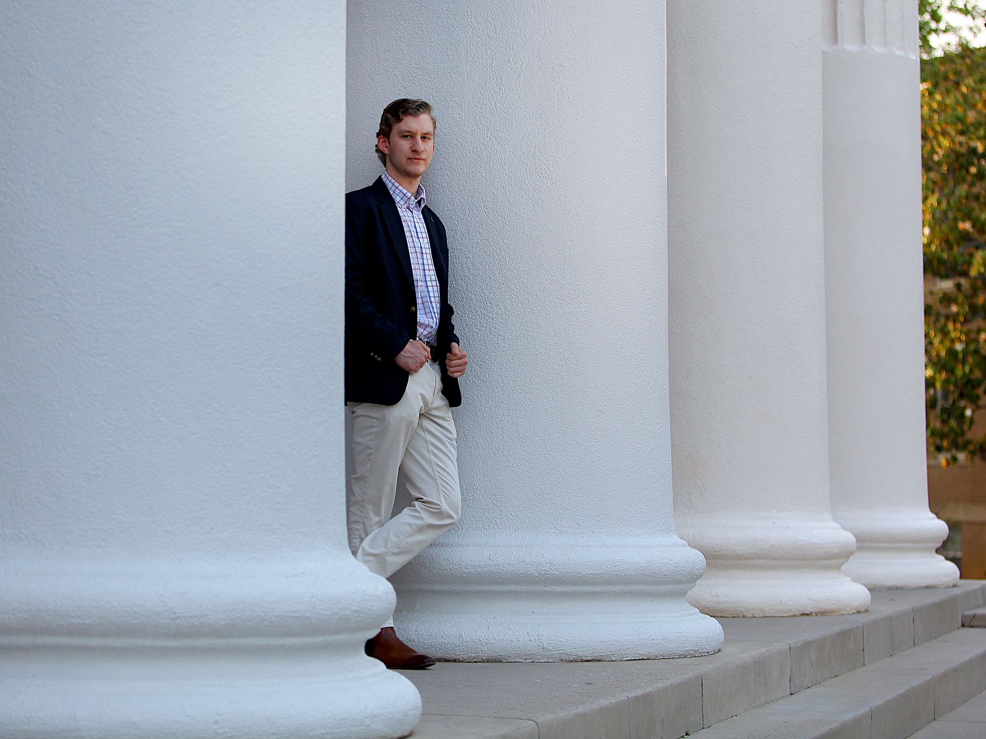 A man is leaning against a row of white columns.