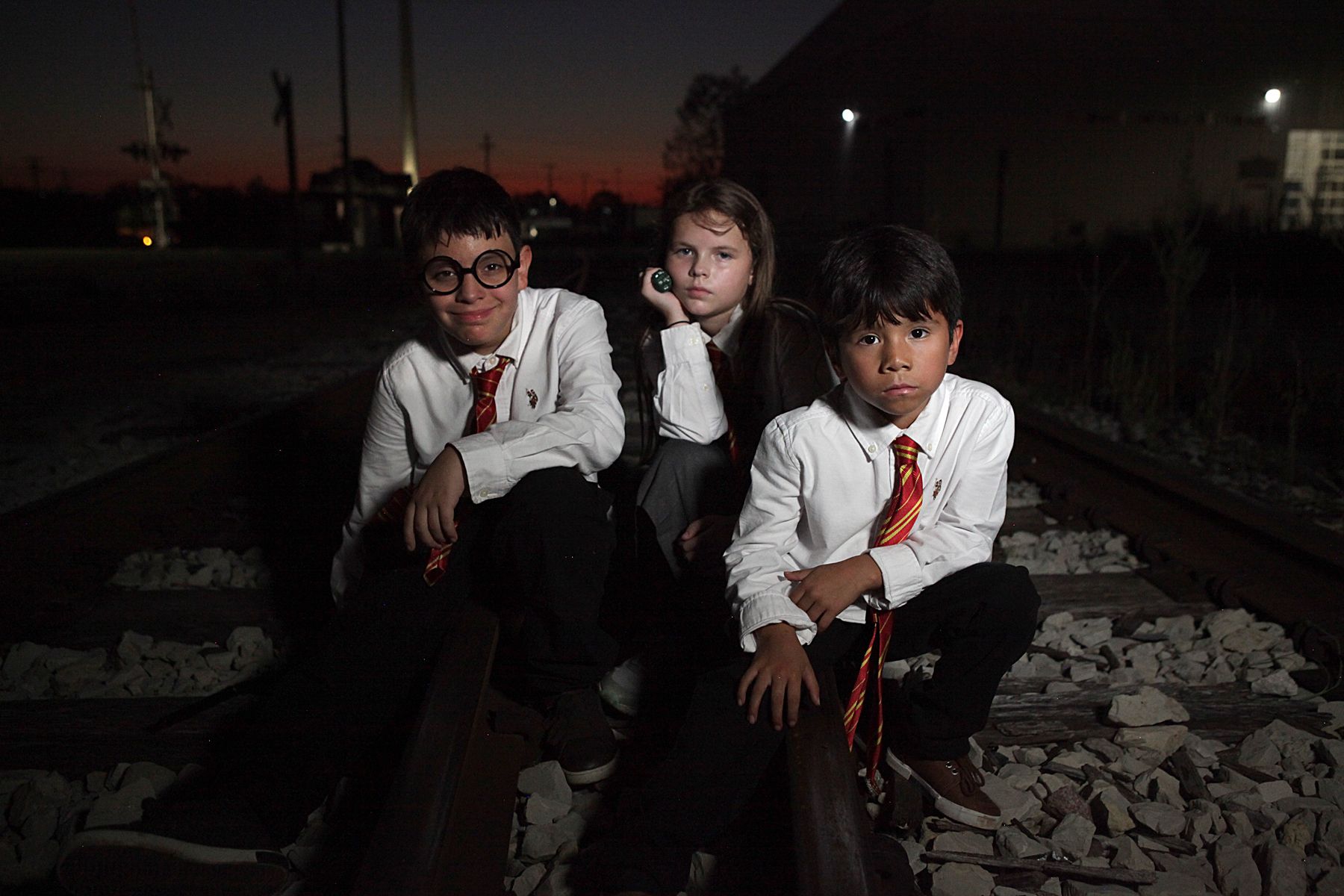 Three children dressed as harry potter are sitting on train tracks.