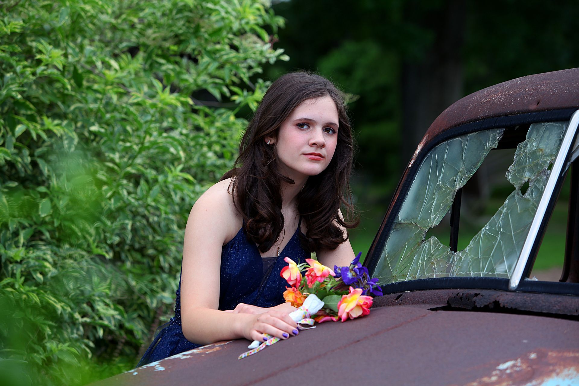 A woman in a blue dress is sitting on the hood of an old rusty truck.