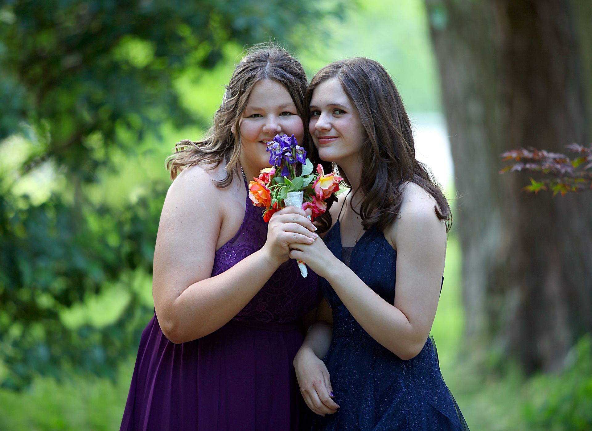 Two bridesmaids are posing for a picture while holding a bouquet of flowers.