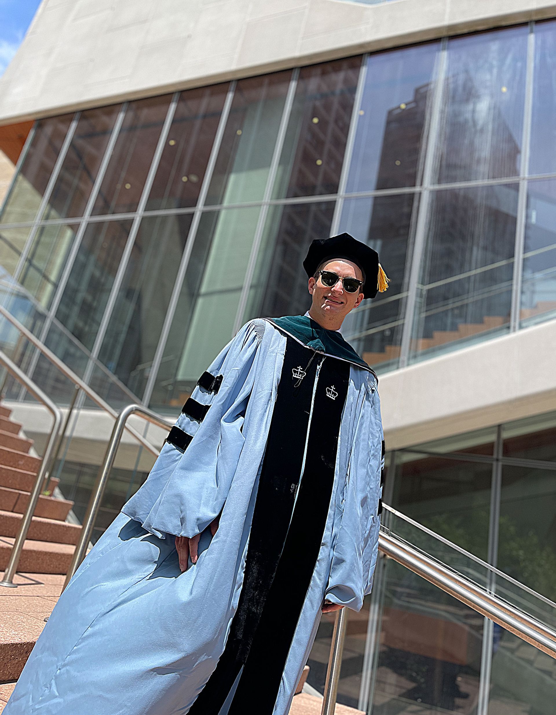 A man in a graduation cap and gown is standing in front of a building.