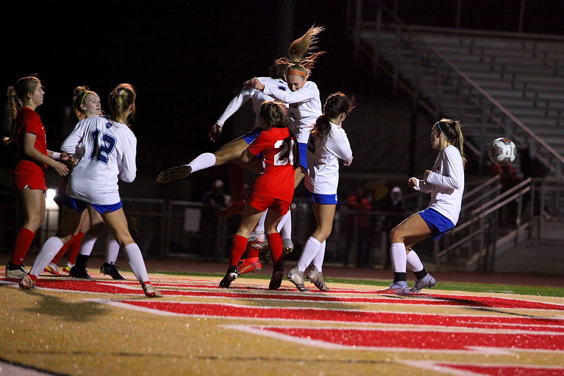A group of girls are playing soccer on a field at night.