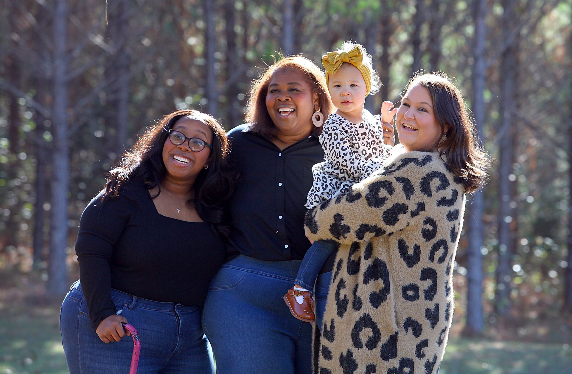 Three women and a baby are posing for a picture in the woods.