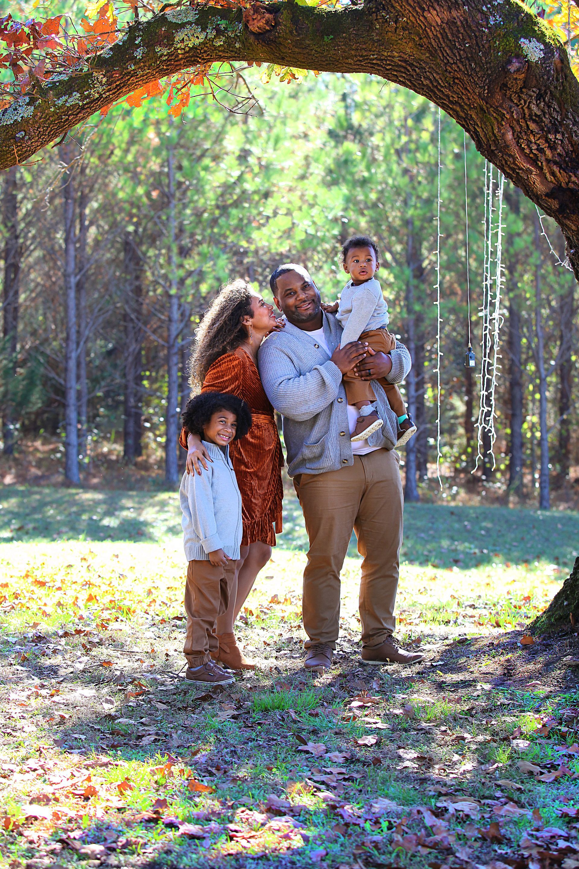 A family is posing for a picture under a tree in the woods.