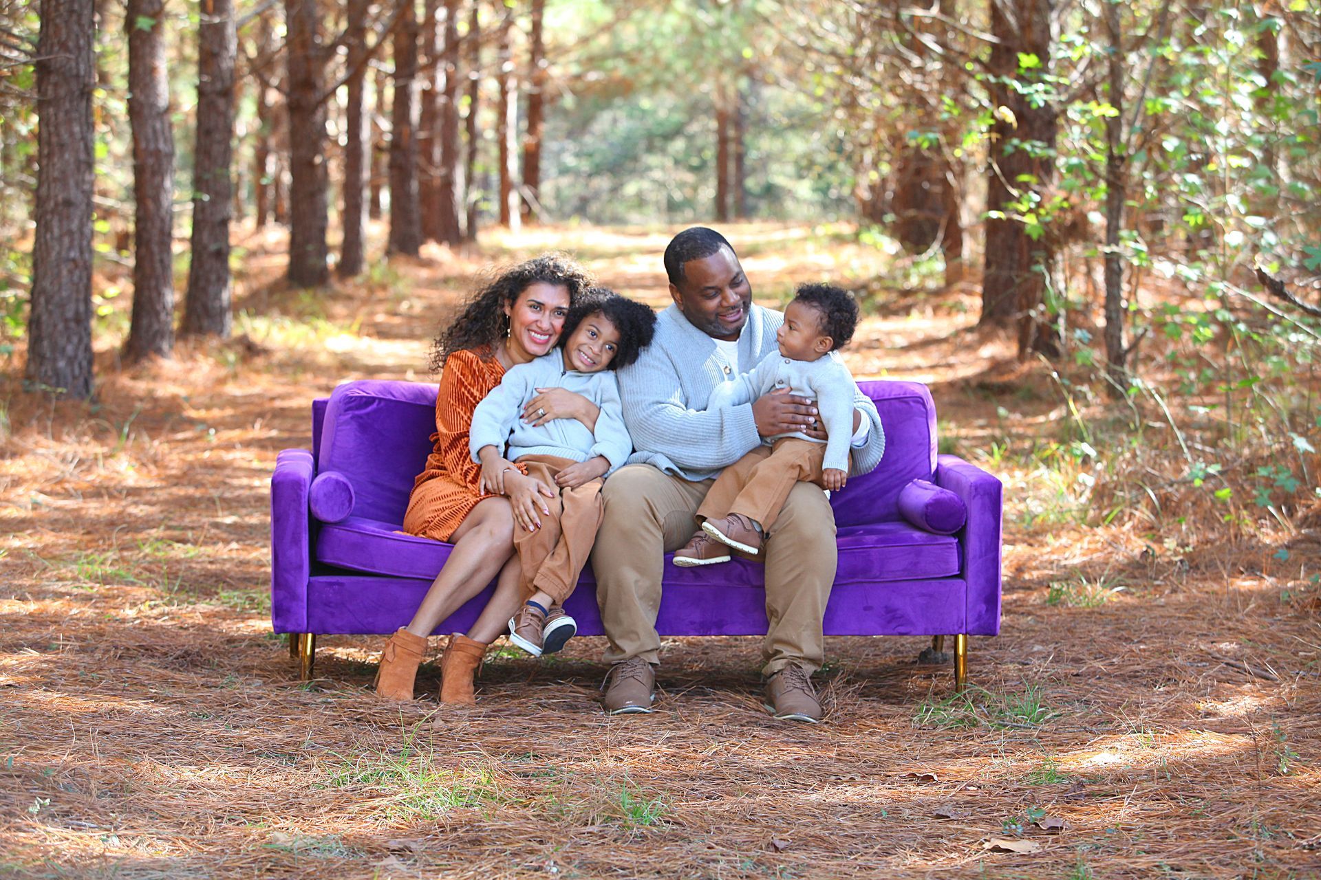 A family is sitting on a purple couch in the woods.