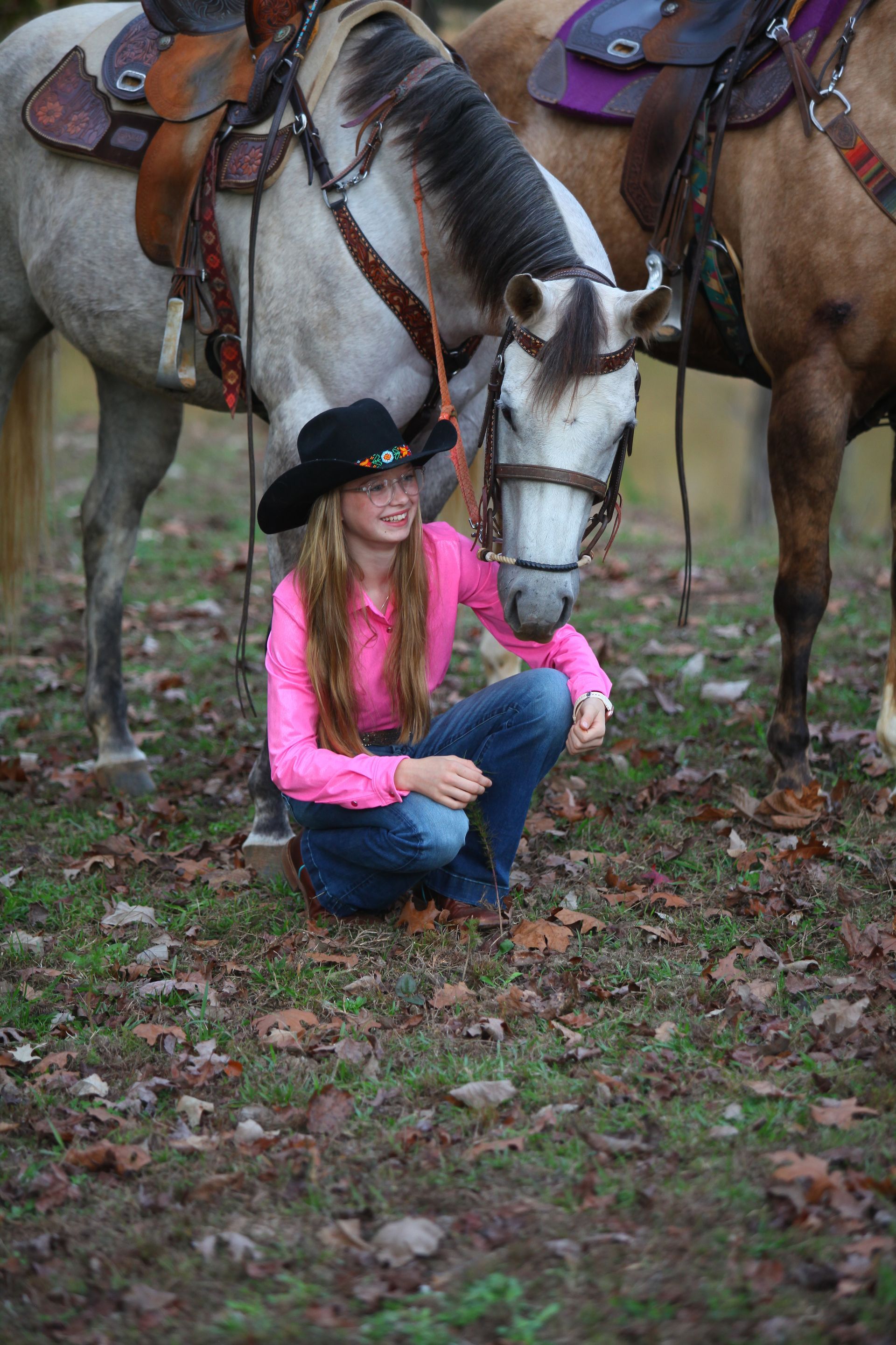 A young girl is kneeling down next to a horse in a field.