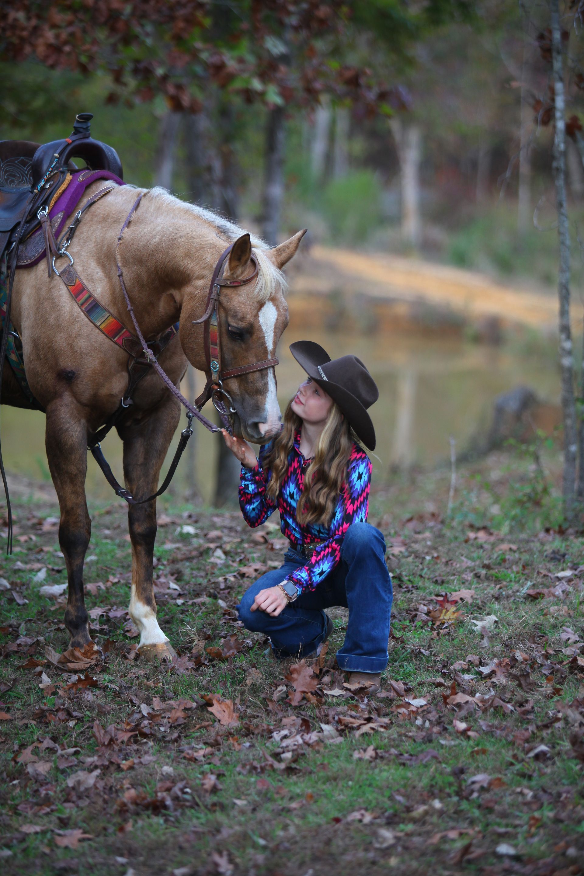 A woman in a cowboy hat is kneeling down next to a horse.