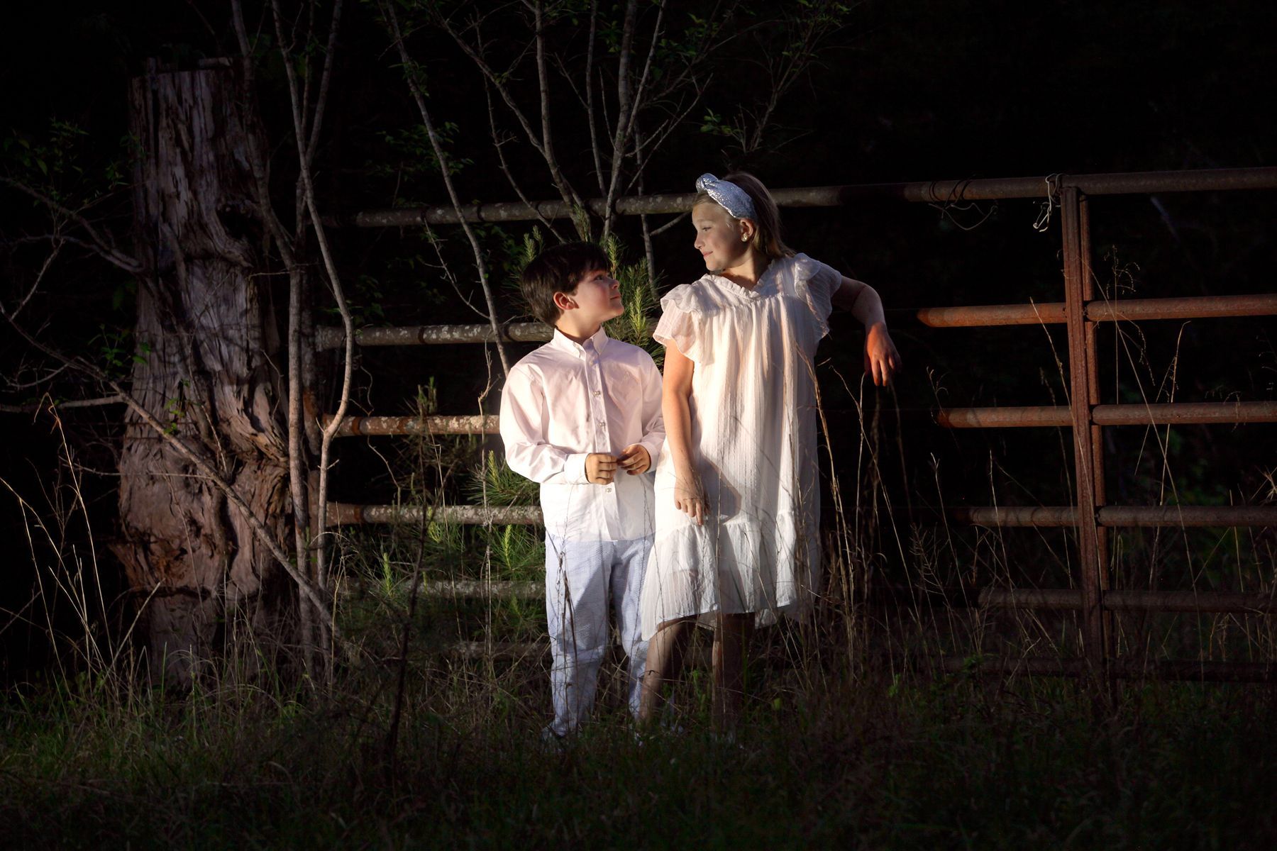 A boy and a girl are standing next to each other in a field at night.