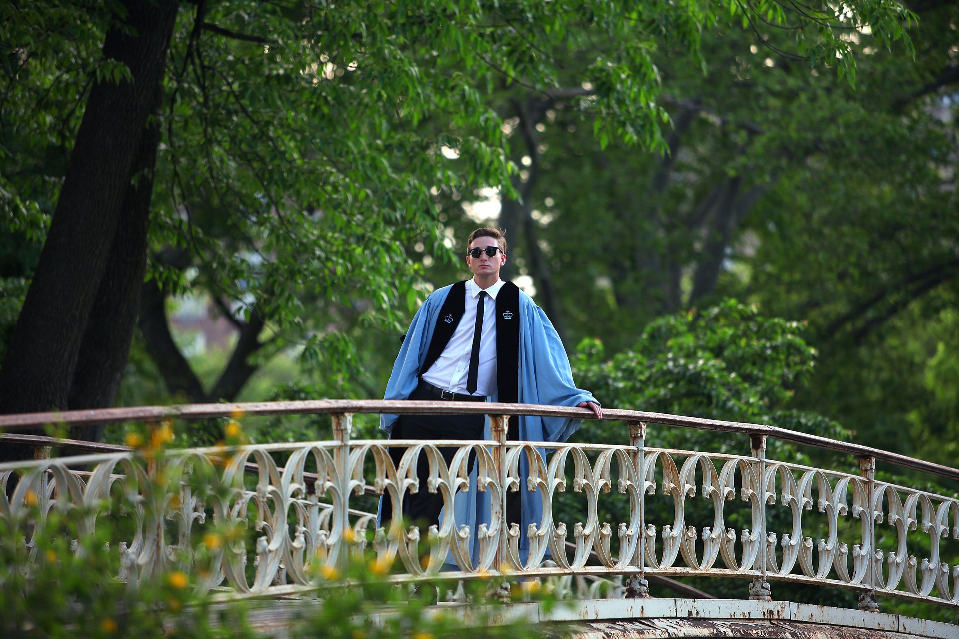 A man in graduation robes is standing on a bridge.