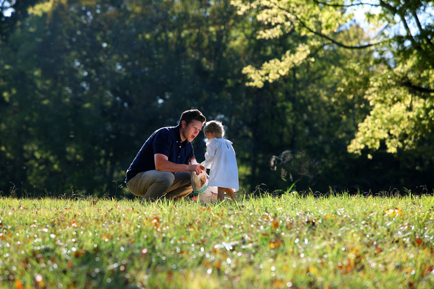 A man and a little girl are kneeling in the grass in a park.