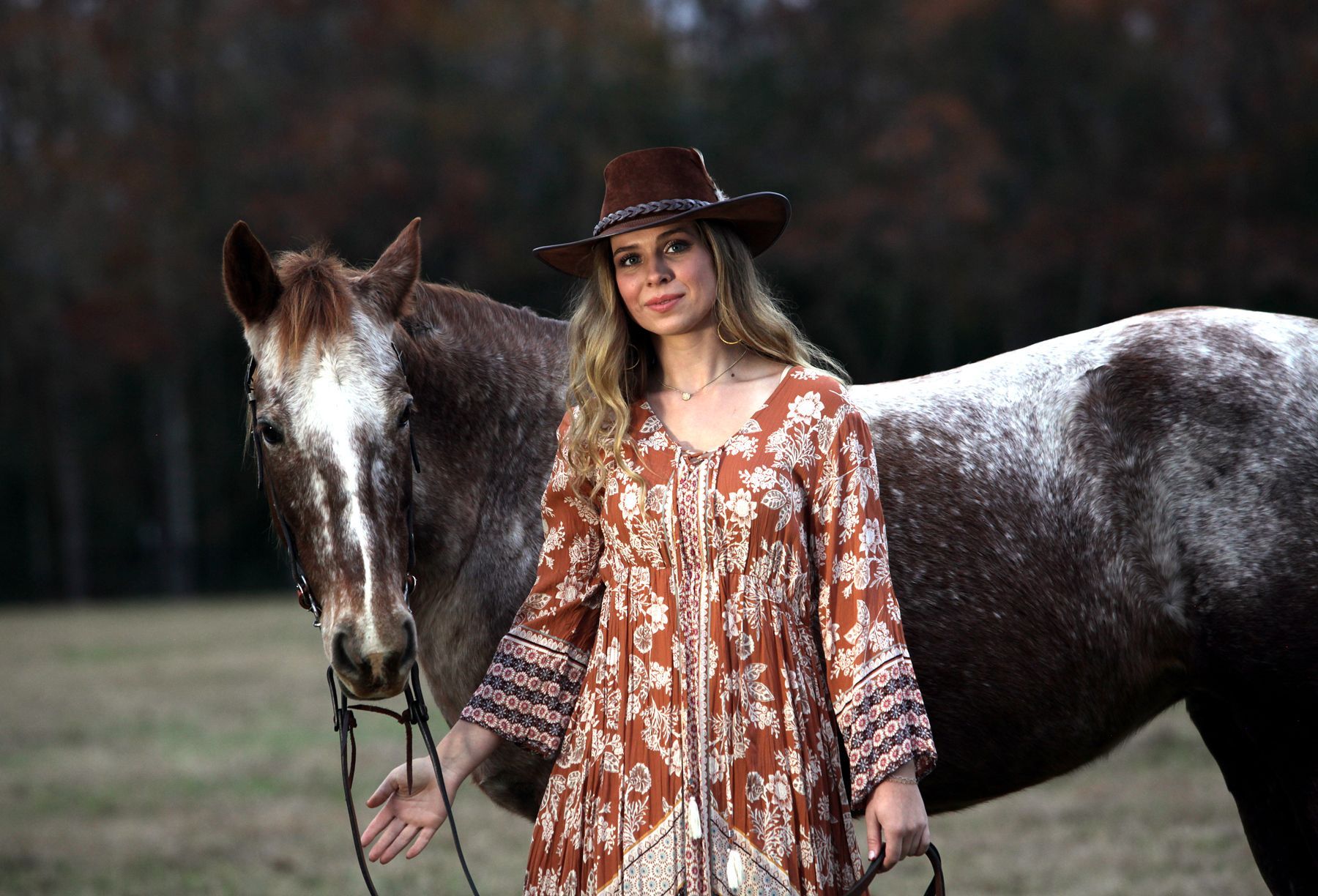 A woman in a cowboy hat is standing next to a horse in a field.