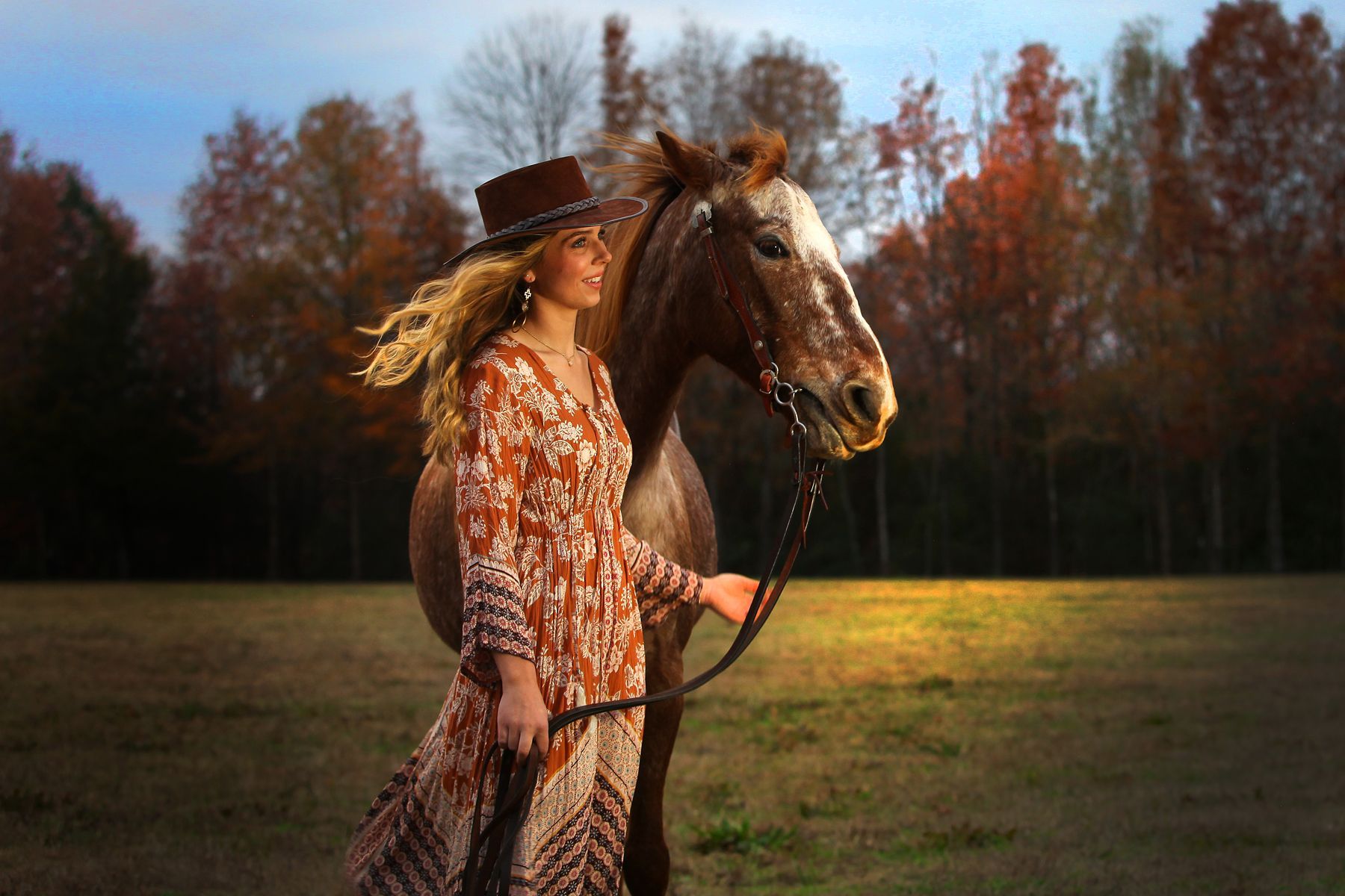 A woman is walking with a horse in a field.