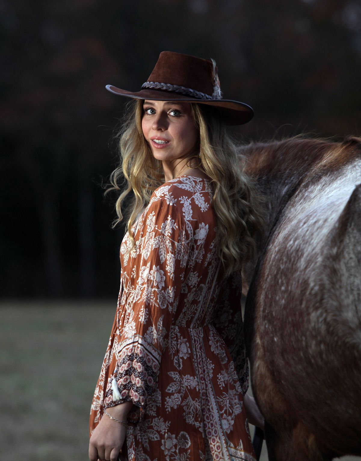 A woman wearing a cowboy hat is standing next to a brown horse.