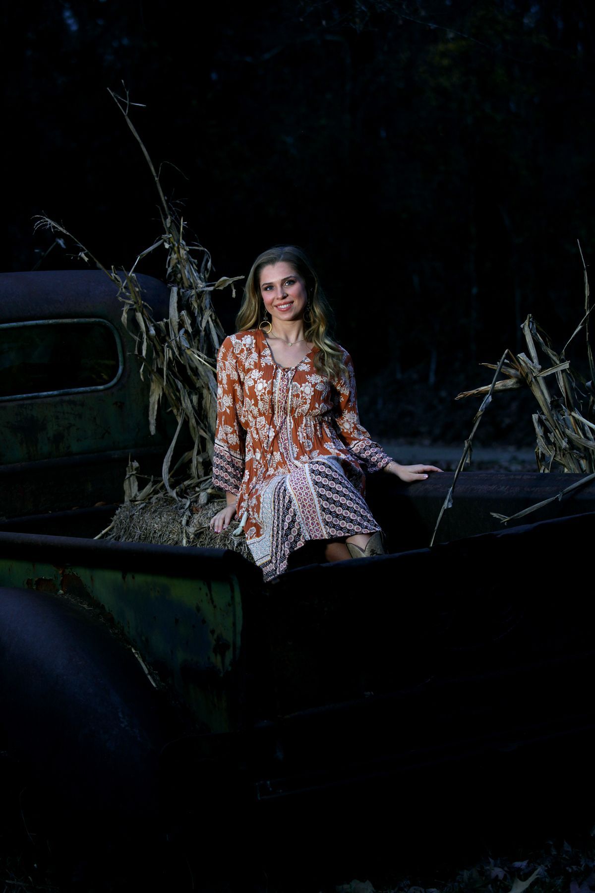 A woman in a dress is sitting on the back of an old truck.