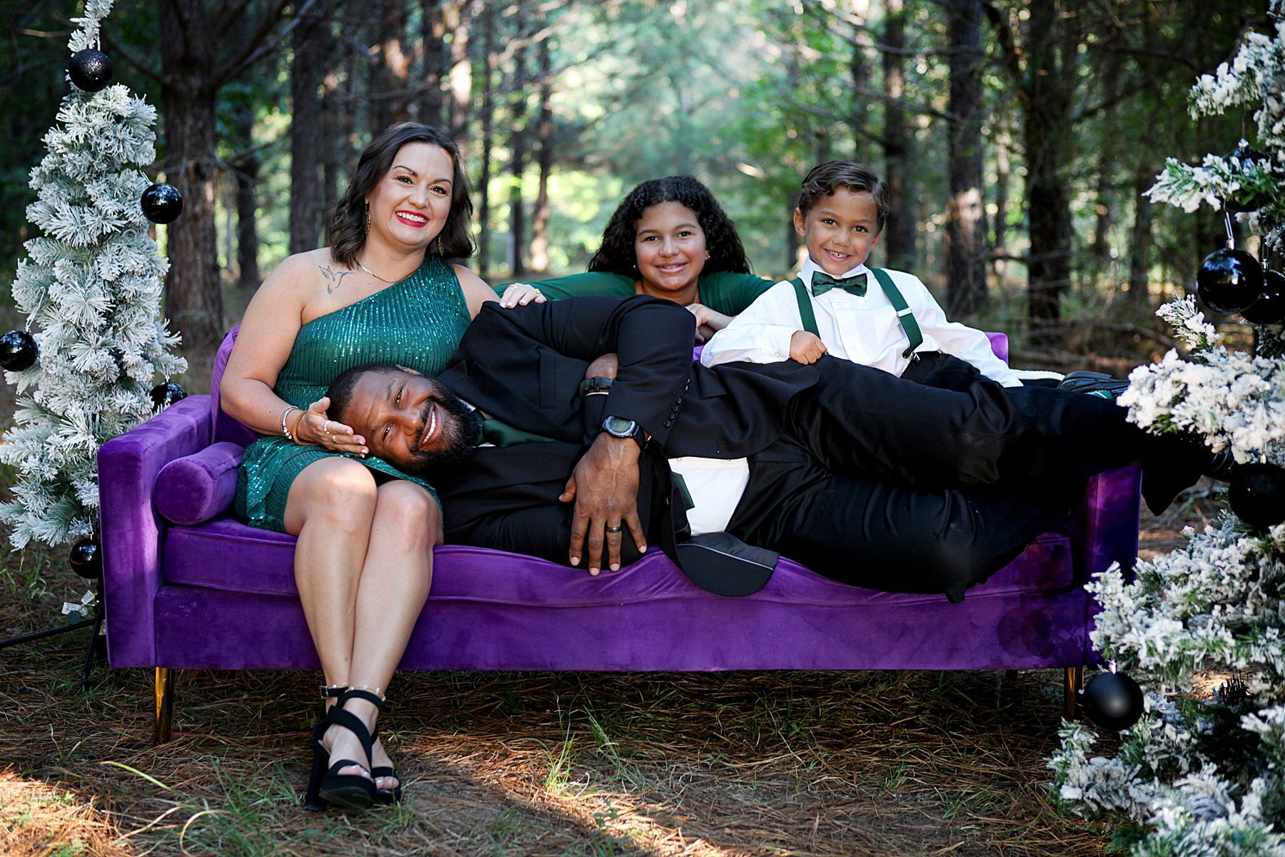 A family is sitting on a purple couch in the woods.
