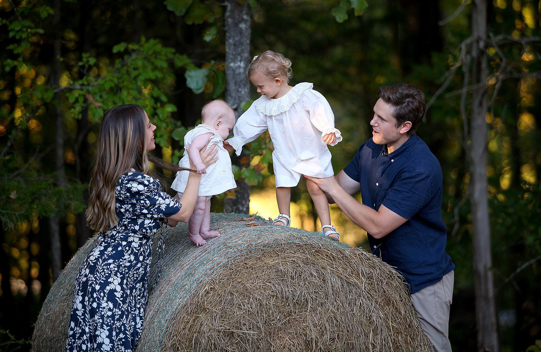A family is standing on top of a bale of hay.
