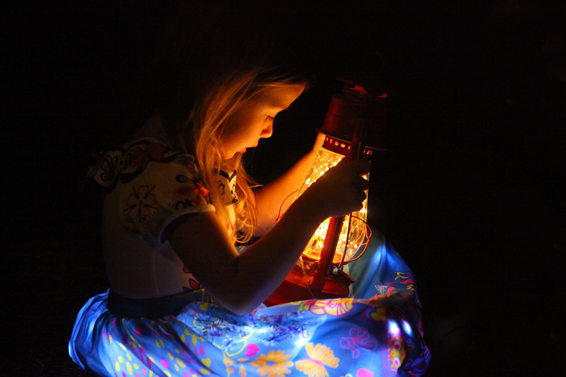 A little girl is playing with a lantern in the dark.