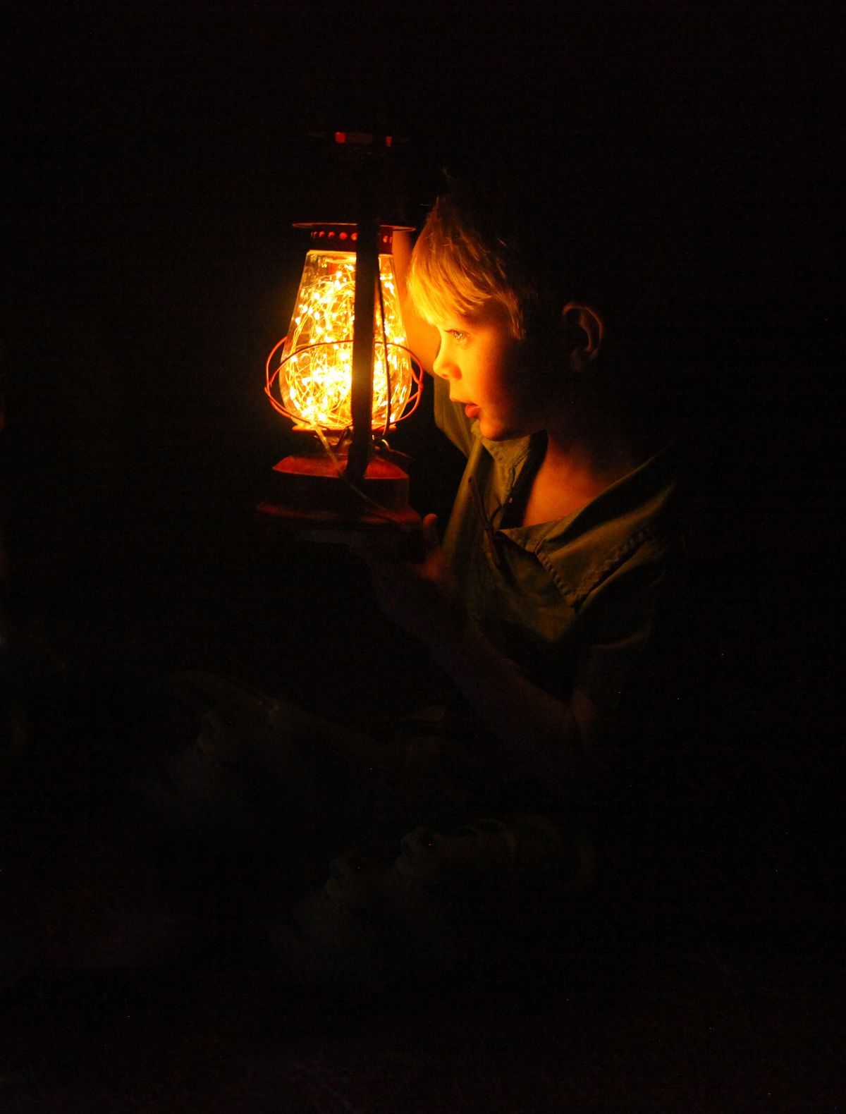 A young boy is looking at a lantern in the dark.