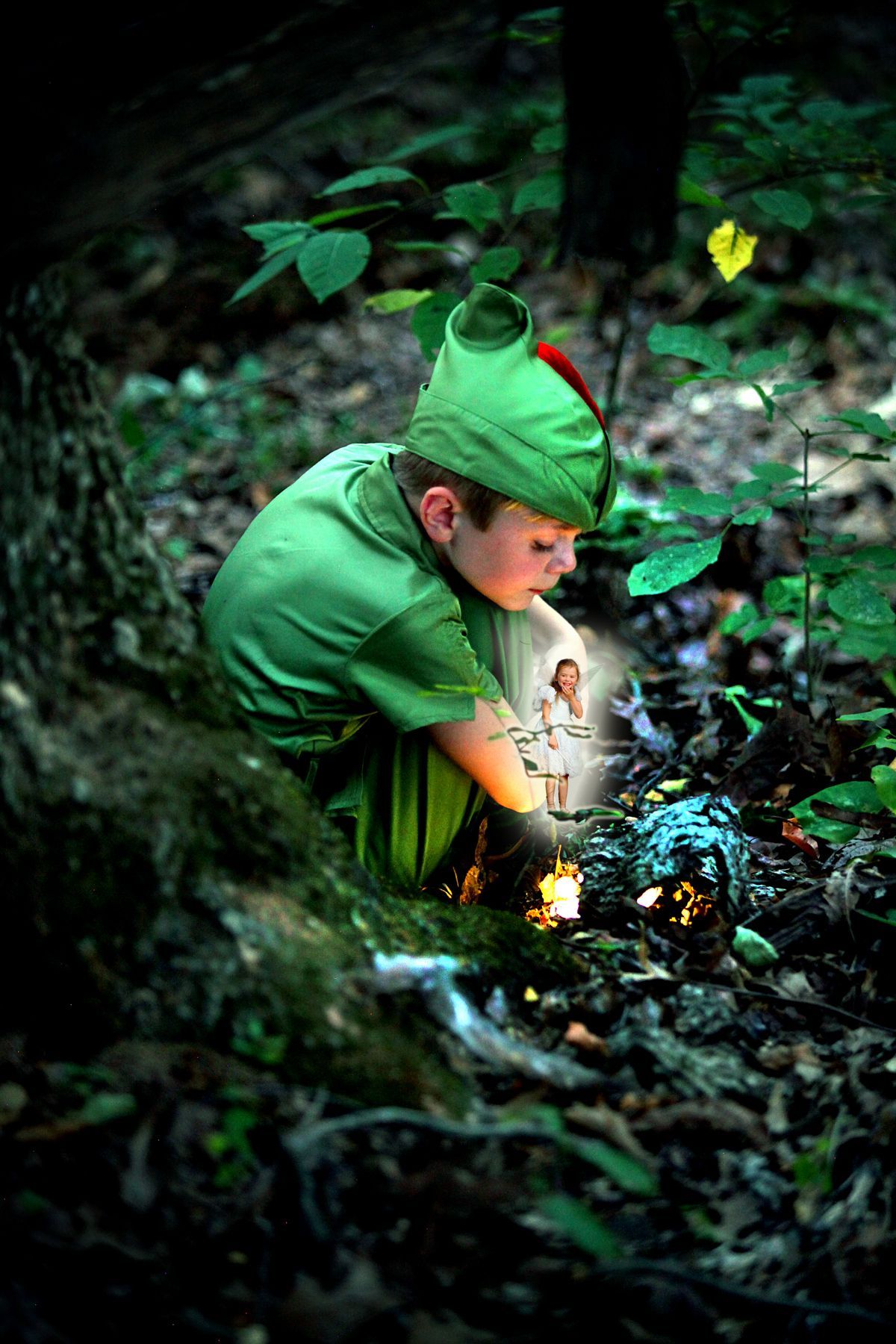 A young boy dressed as peter pan is sitting under a tree in the woods.