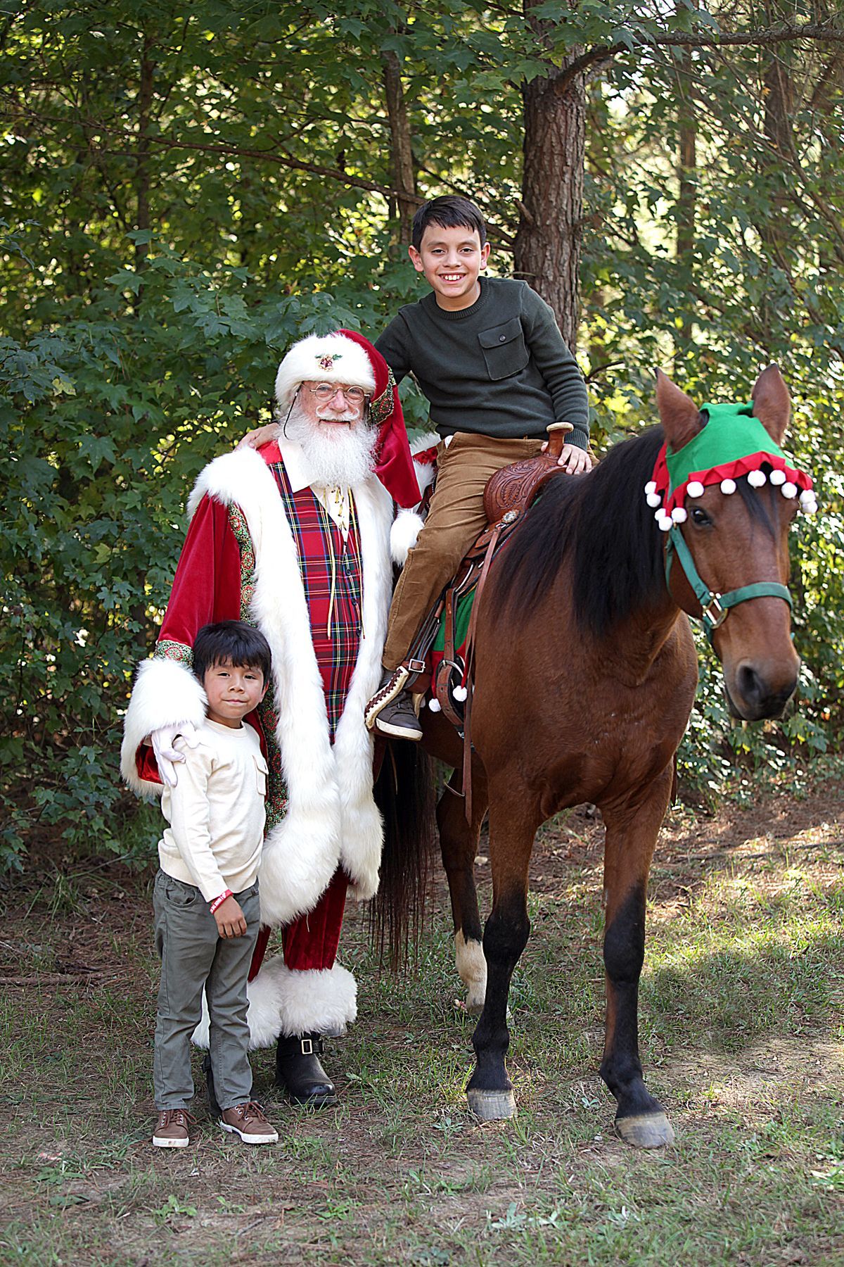 Santa claus is riding a horse with two children standing next to him.