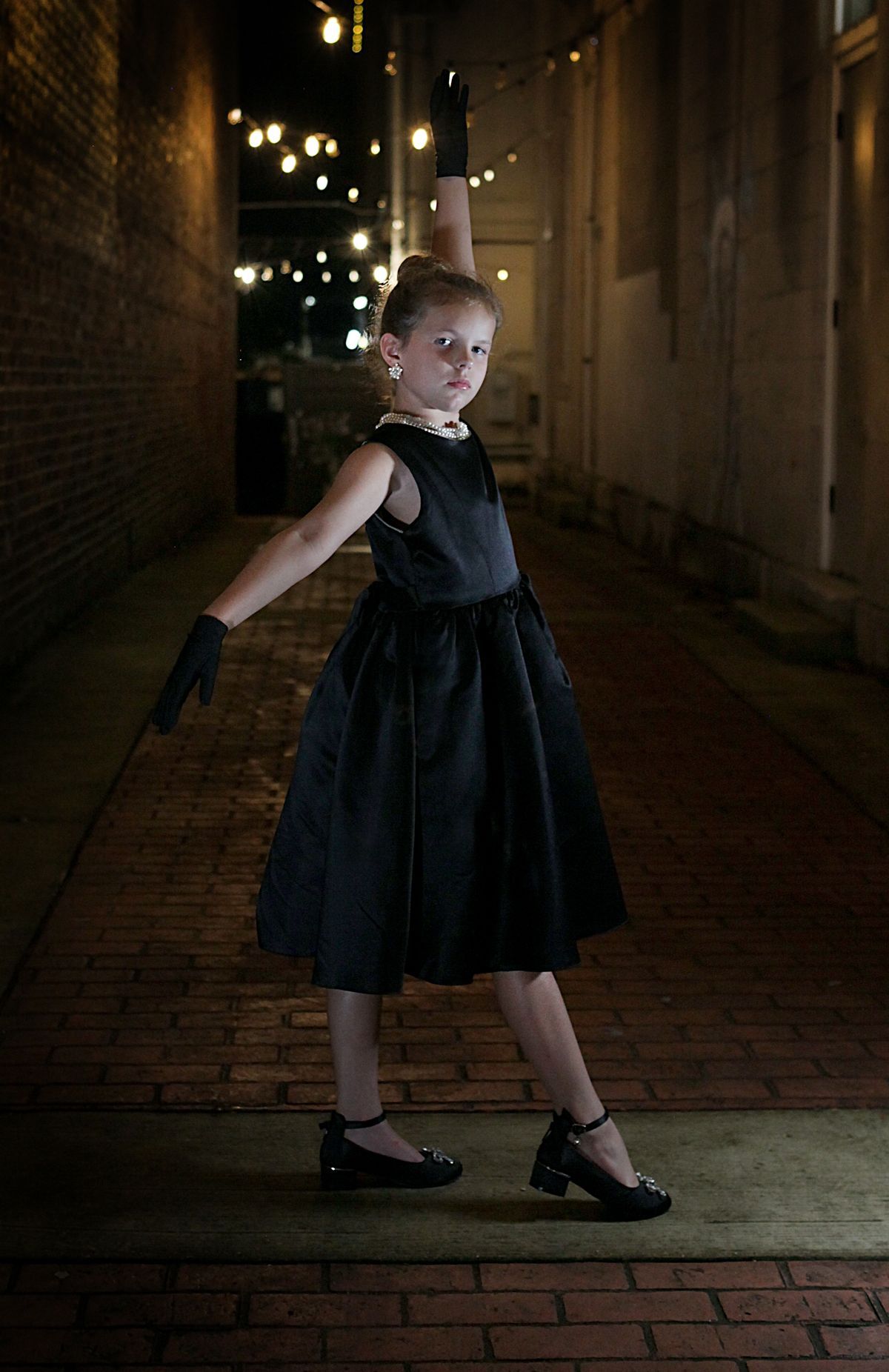A little girl is wearing a black dress and black gloves.