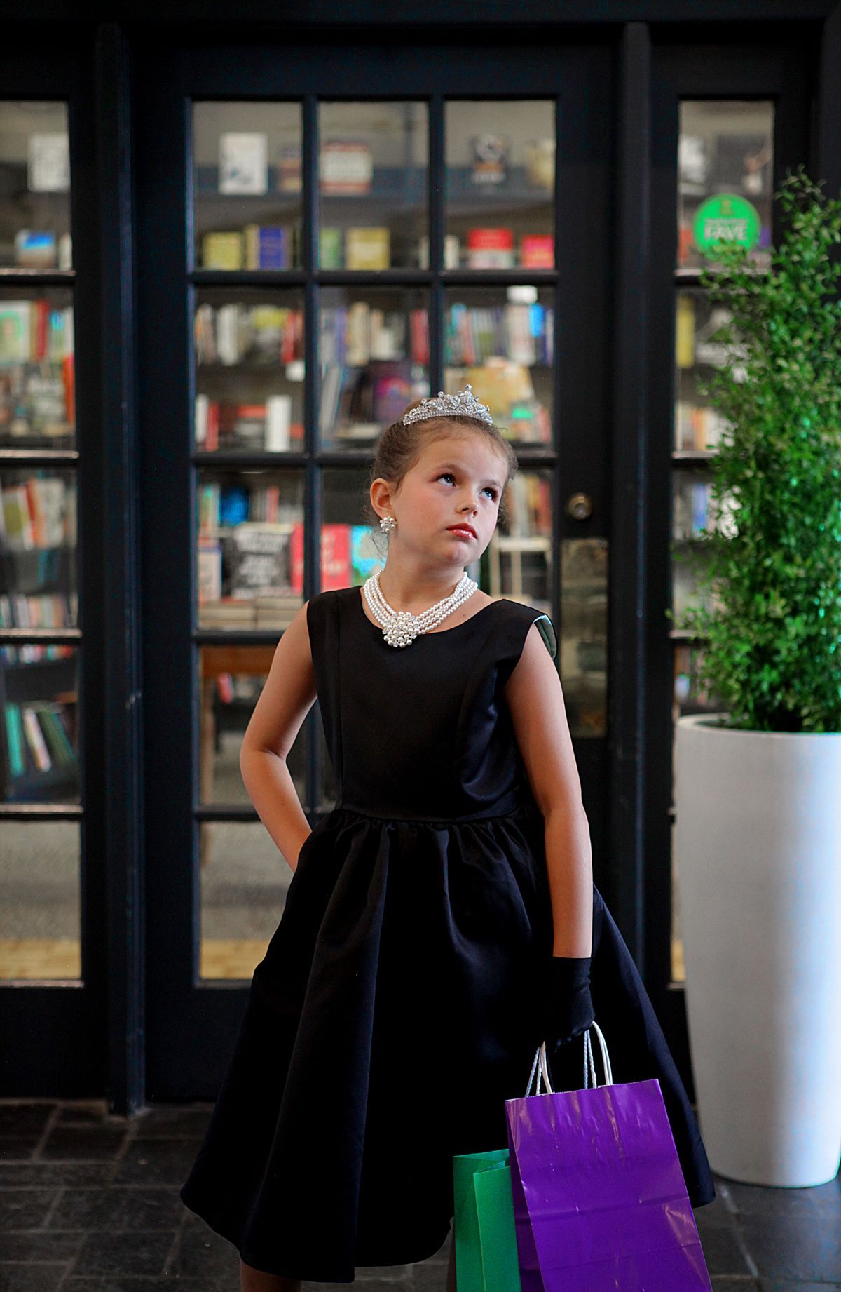 A little girl in a black dress is holding shopping bags.