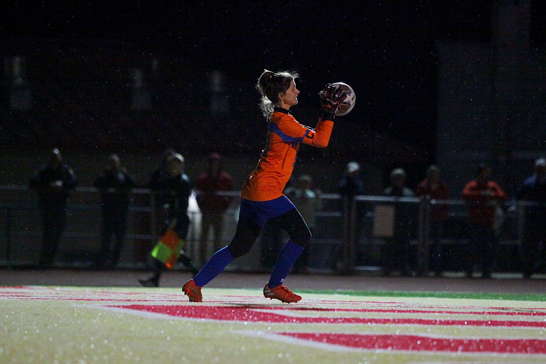 A keeper is catching a soccer ball on a field at night.