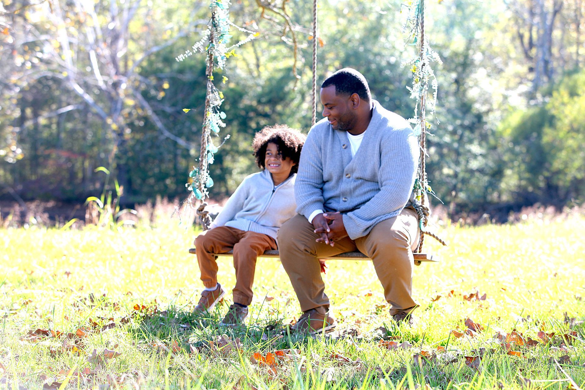 A man and a boy are sitting on a swing in a field.