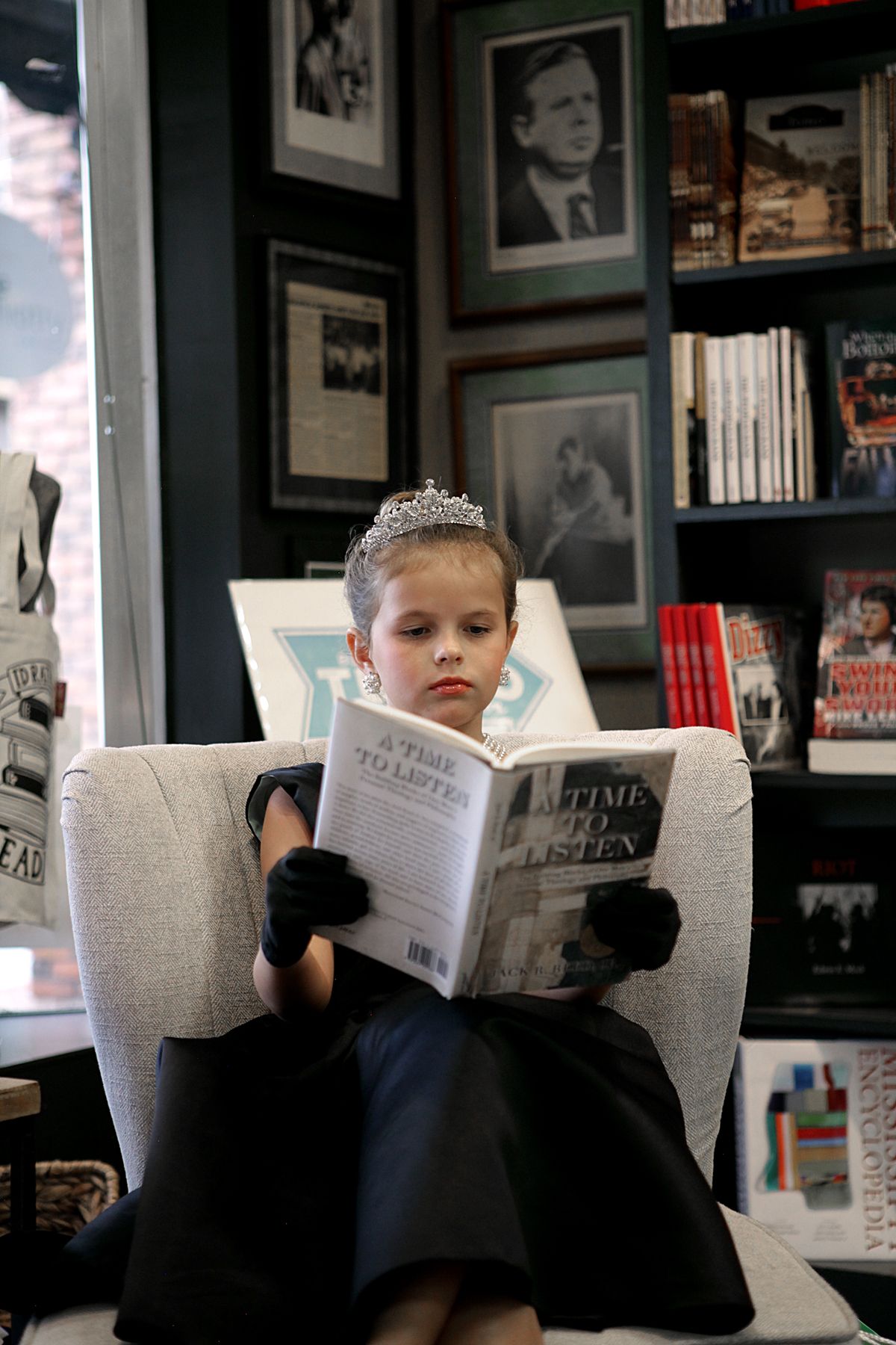 A little girl is sitting in a chair reading a book.