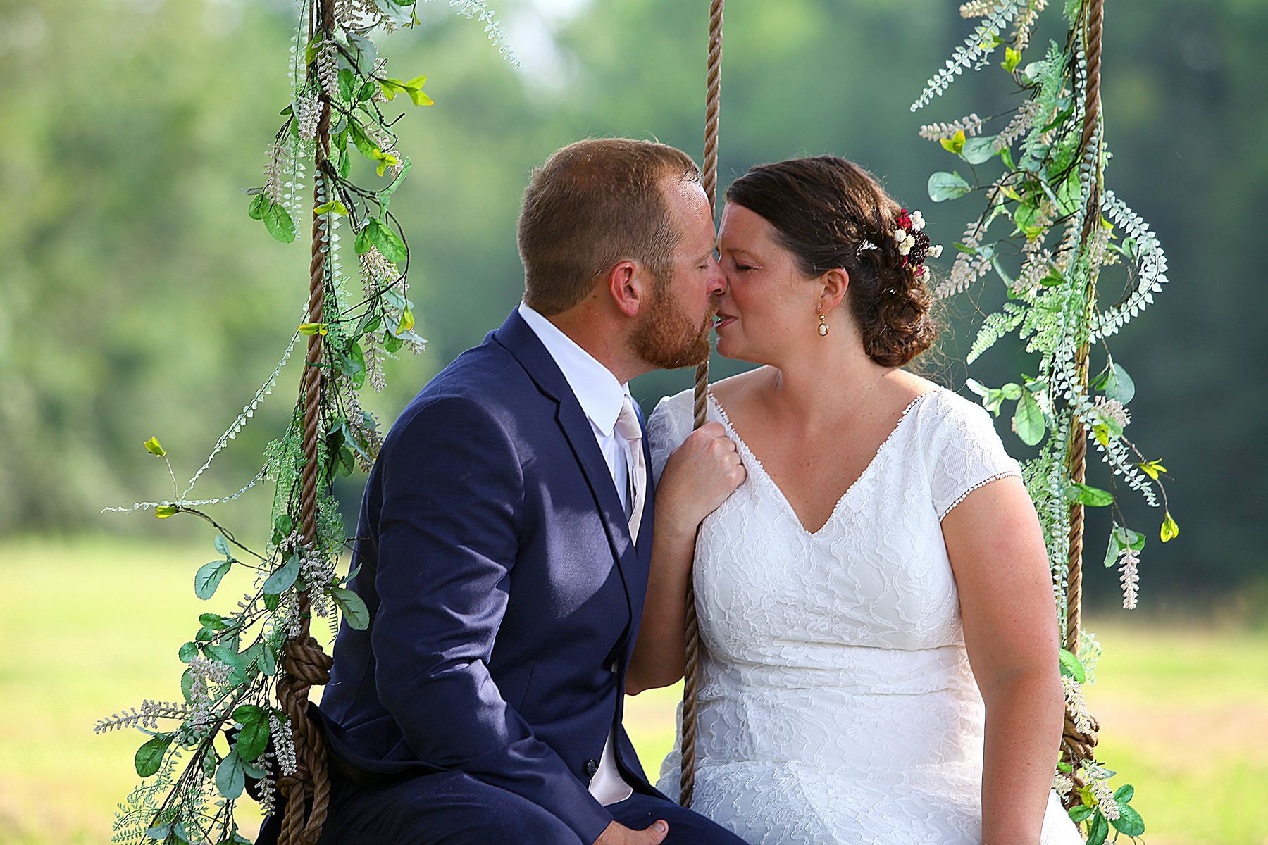 A bride and groom are kissing while sitting on a swing.