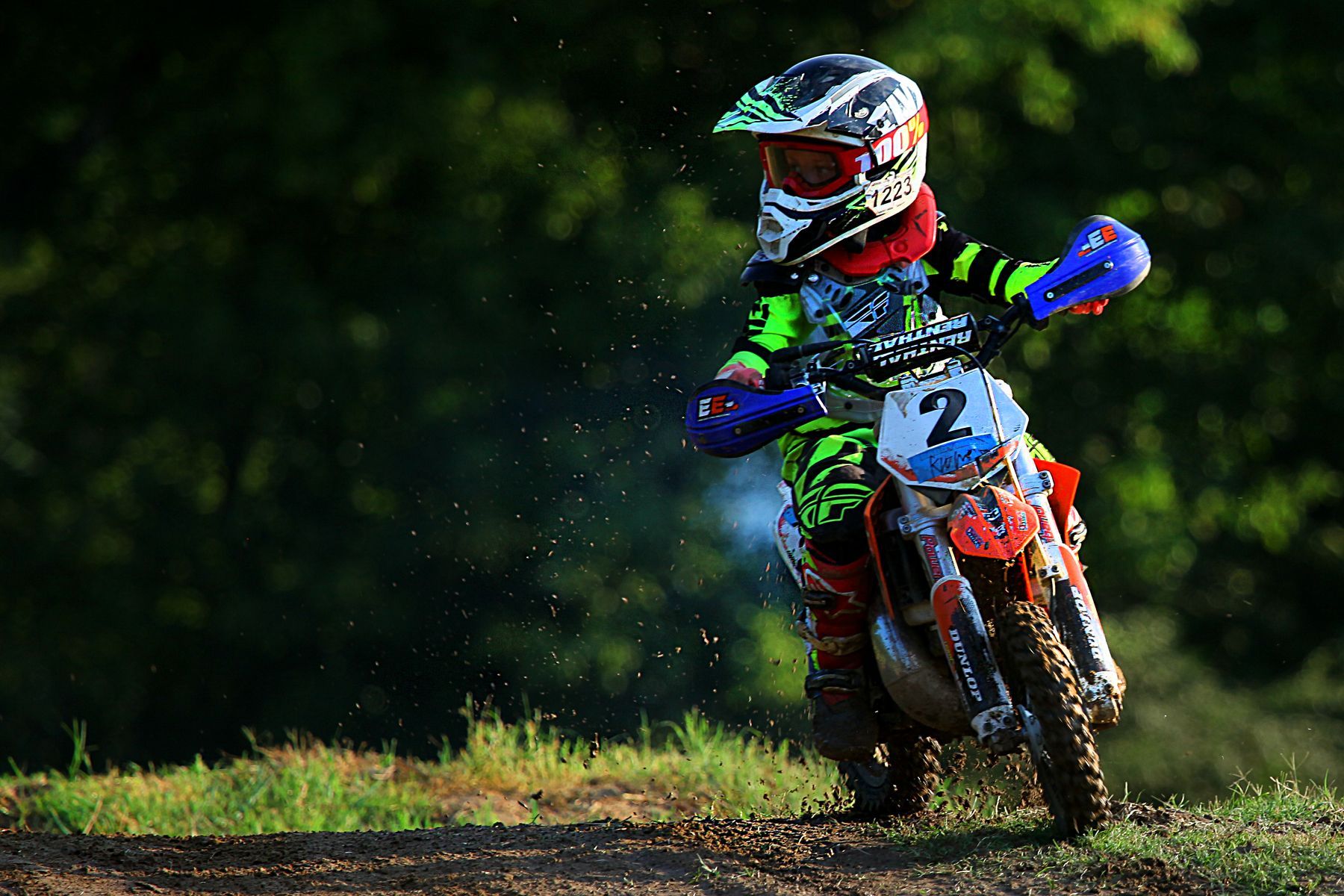 A young boy is riding a dirt bike on a dirt road.