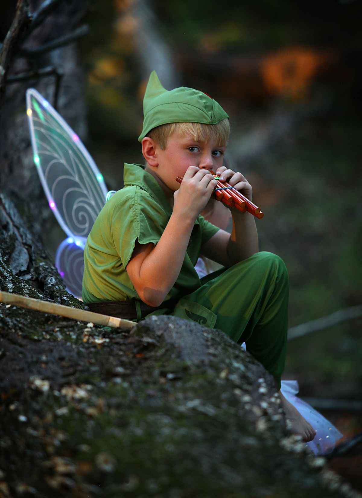 A young boy dressed as Peter Pan is playing a flute