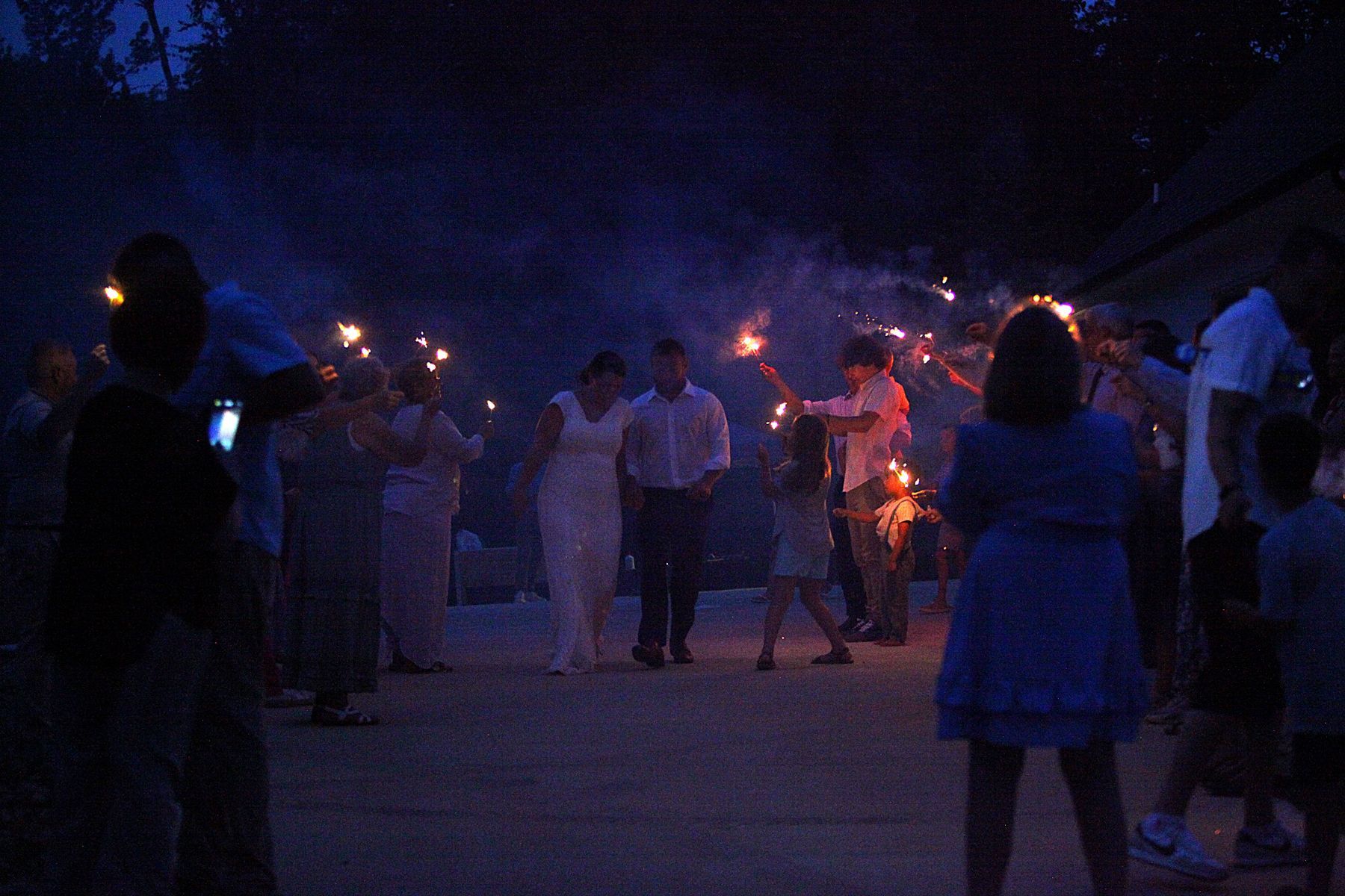 A group of people are holding sparklers at a wedding reception.