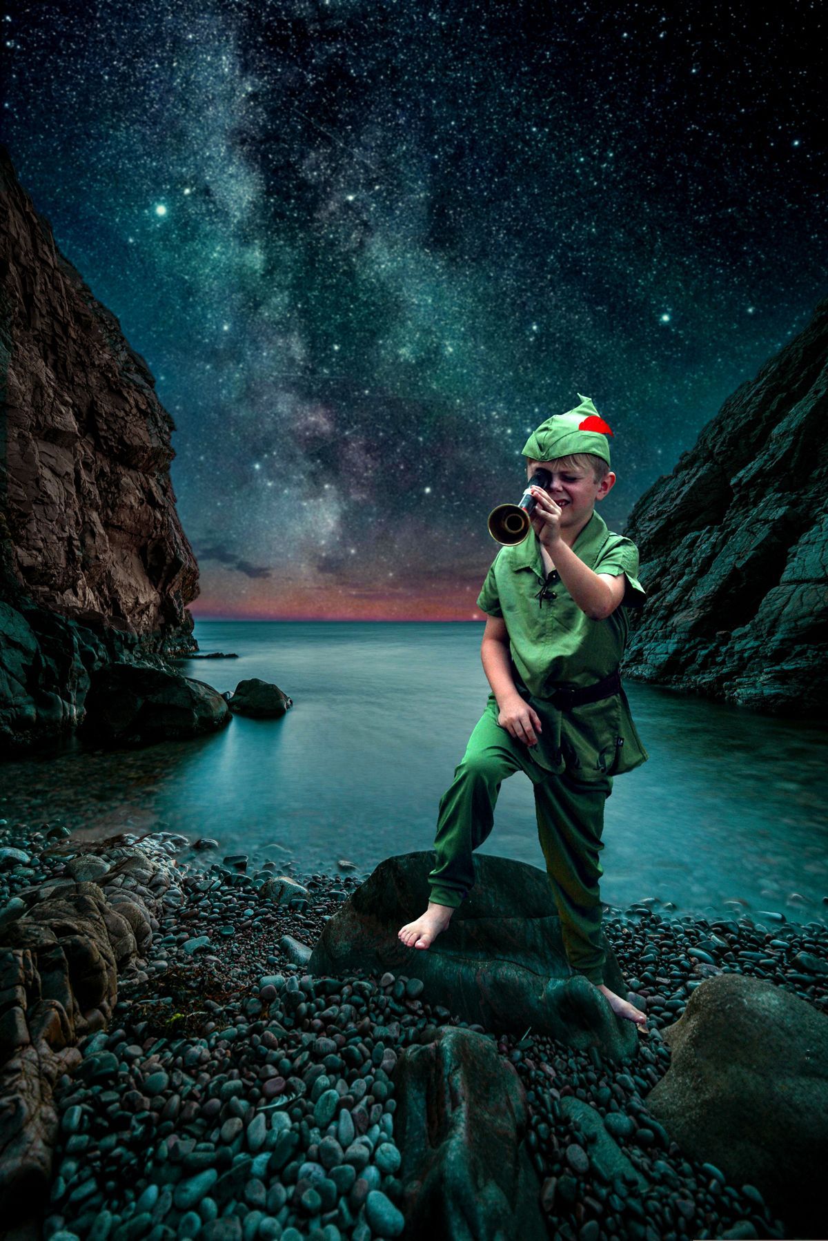 A young boy dressed as peter pan is standing on a rocky beach looking through a telescope.