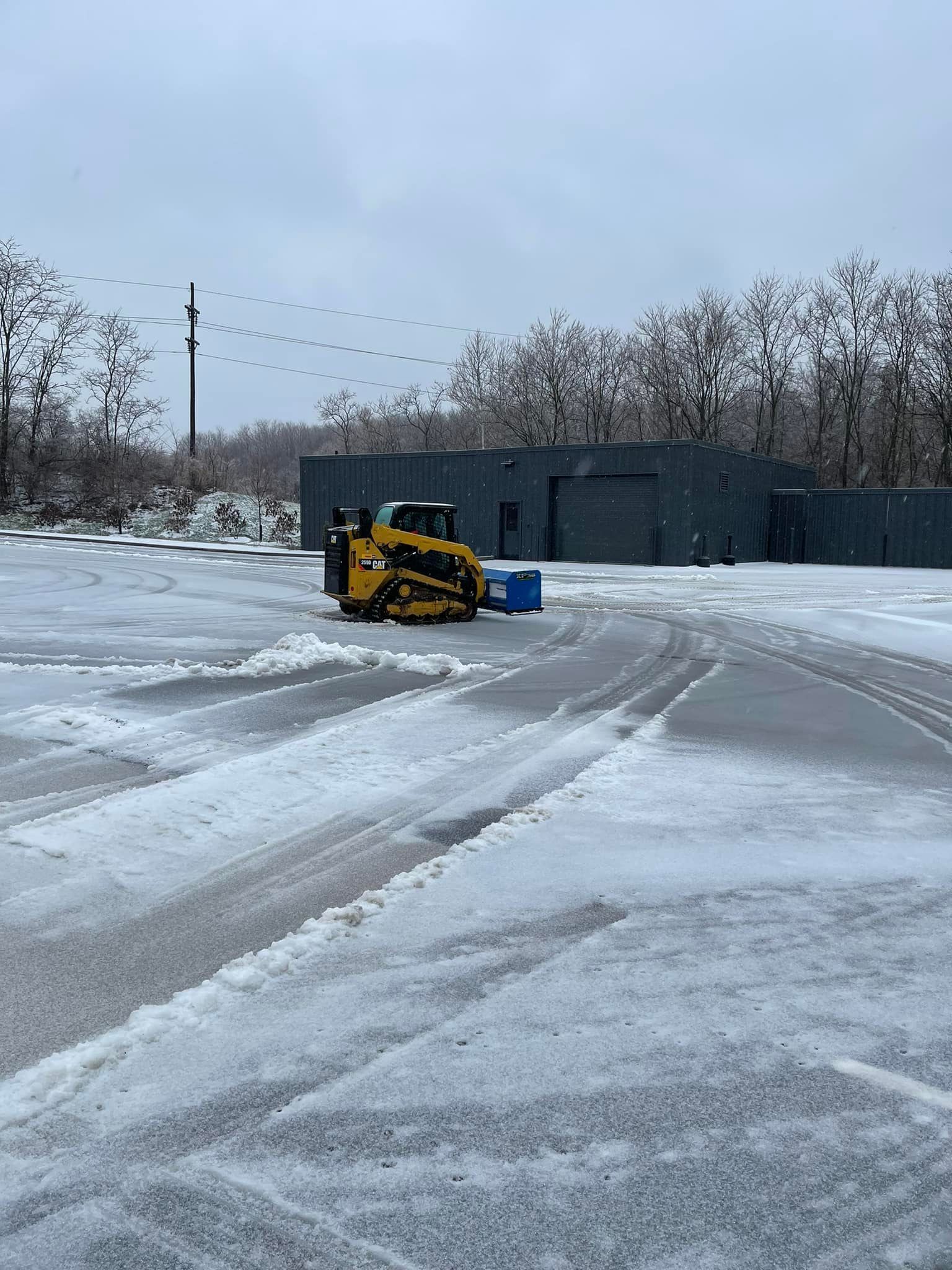 A yellow skid steer clears snow from a parking lot on an overcast day.