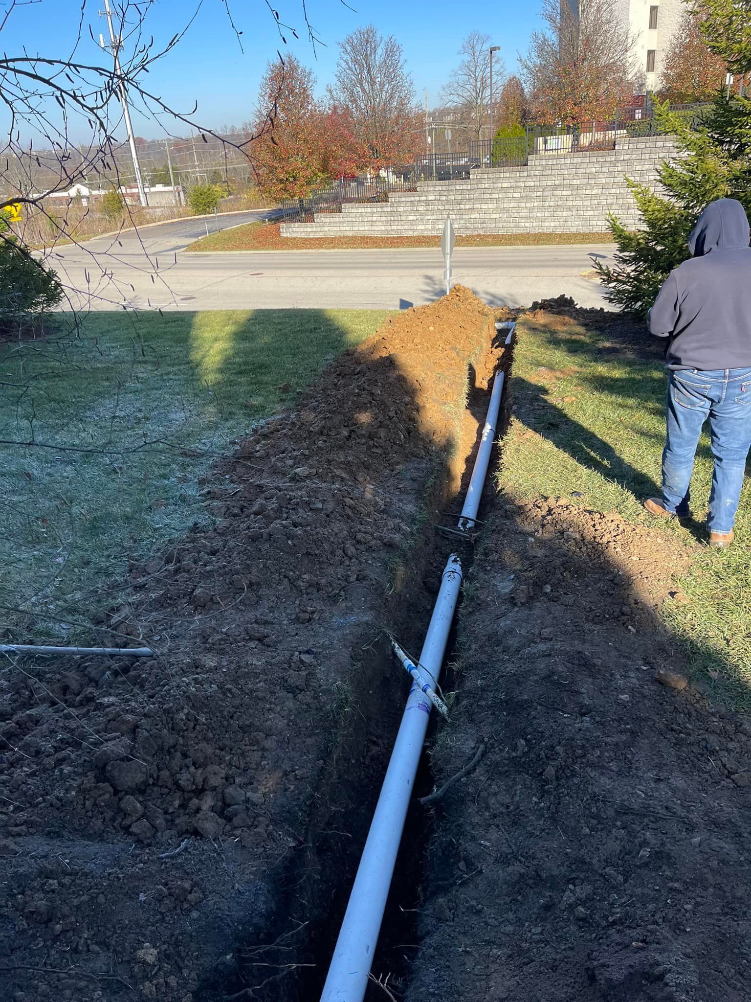 A trench dug in a lawn with PVC pipe running through it. Person standing nearby.