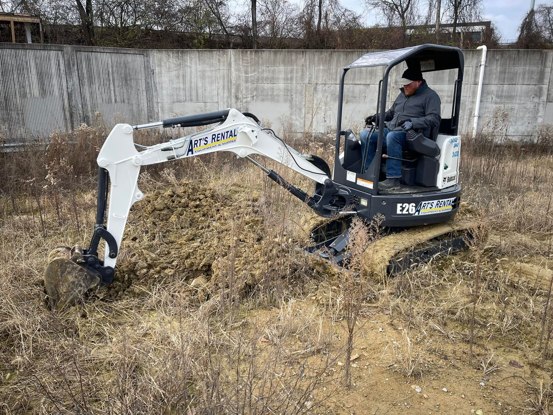 Man operating a Bobcat excavator, digging in a field.