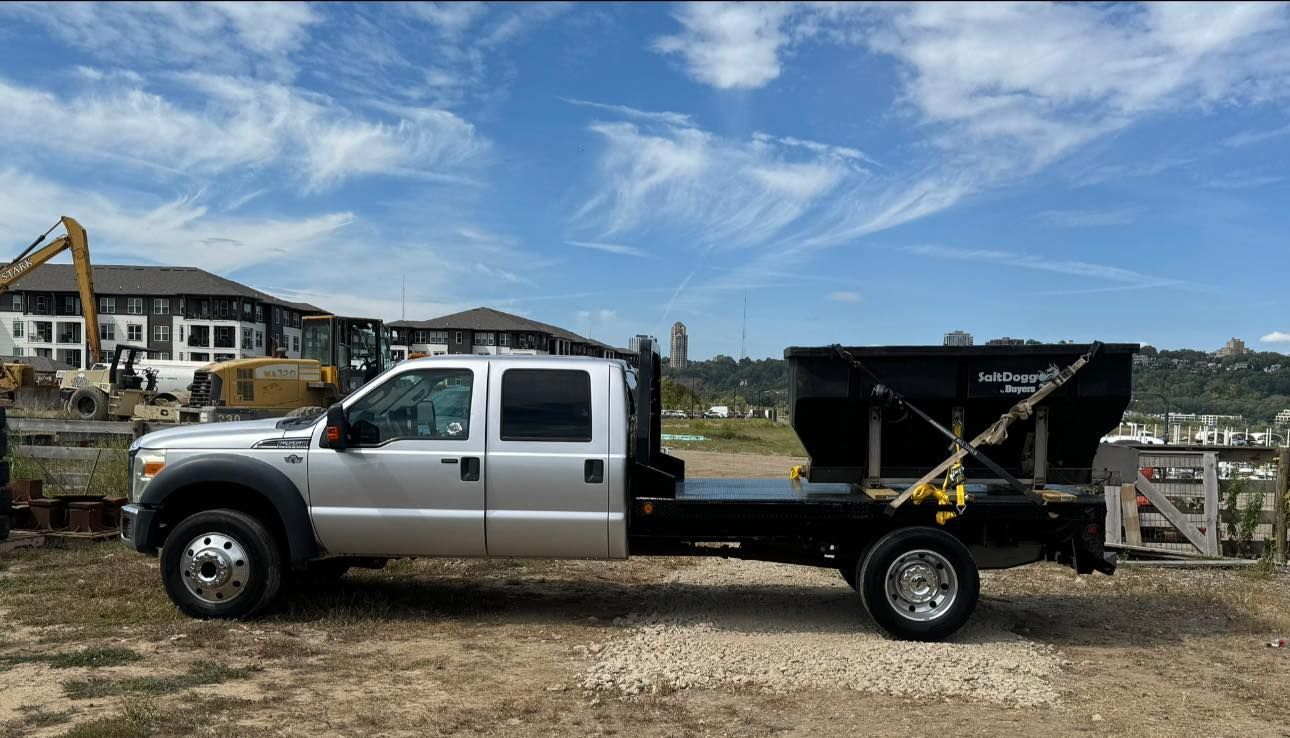 Silver Ford truck with a black flatbed and attached container, parked at a construction site on a sunny day.