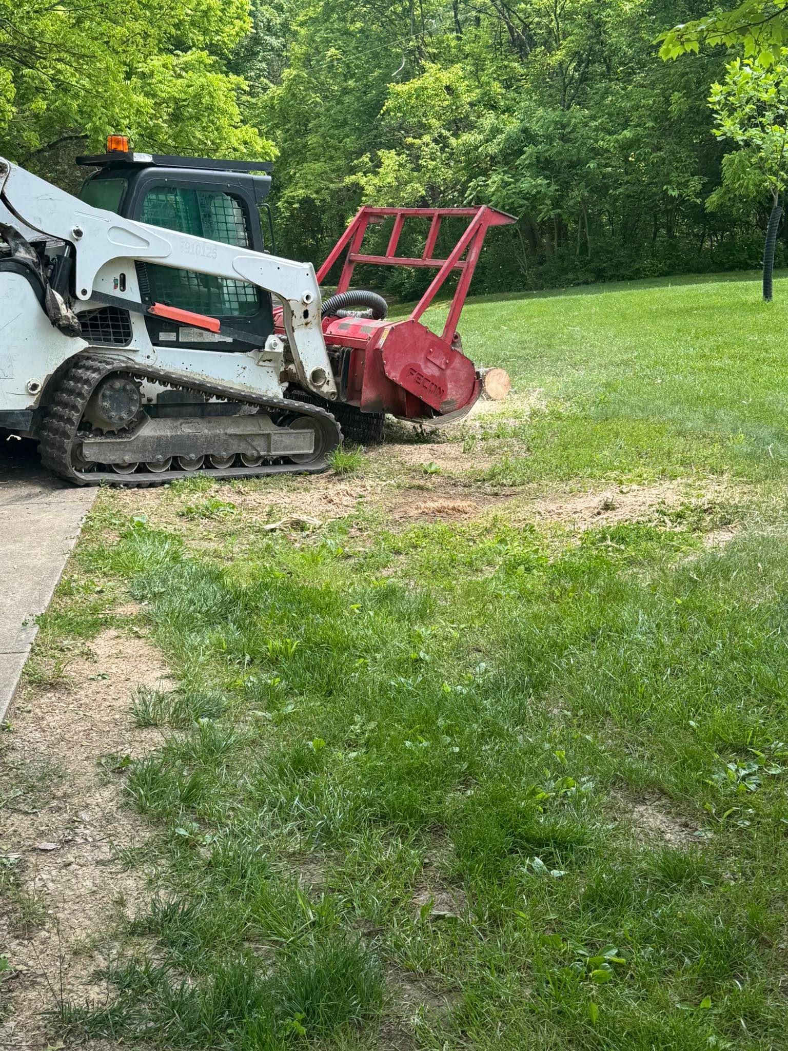 A Bobcat skid steer with a stump grinder grinding a tree stump in a grassy area.