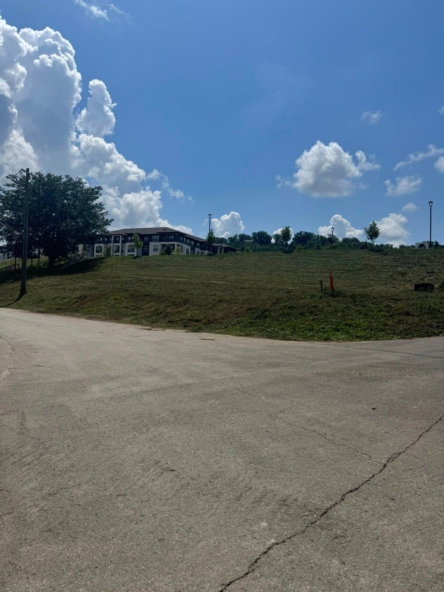 Asphalt road leads to a grassy hill with a building on top under a blue sky with clouds.