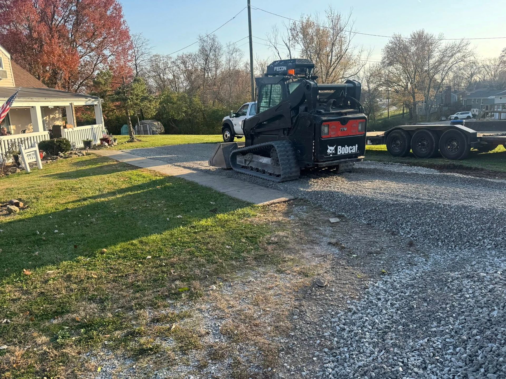 Black Bobcat construction vehicle on gravel driveway near house and trailer.