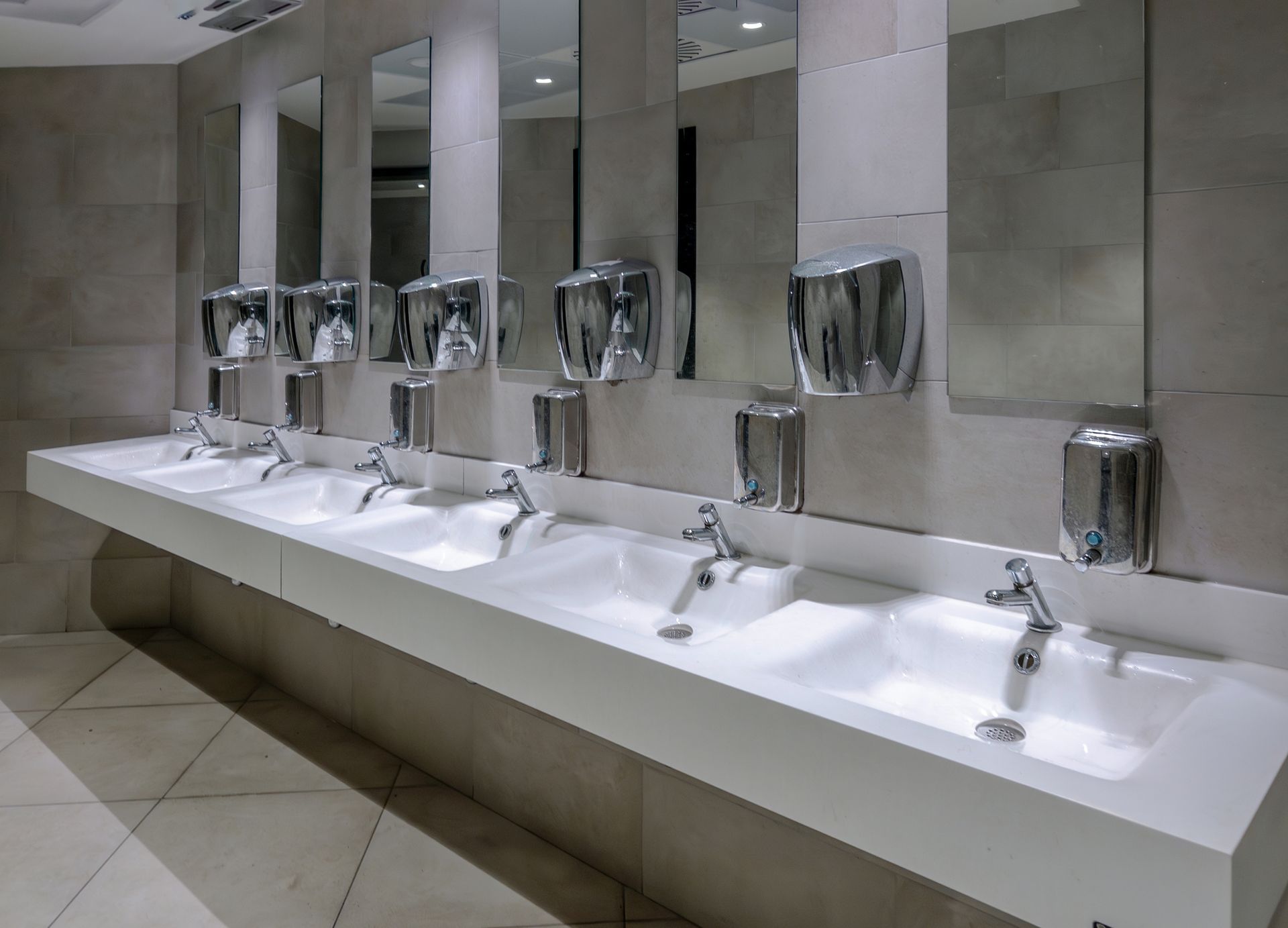 A row of sinks in a public restroom with hand sanitizer dispensers.