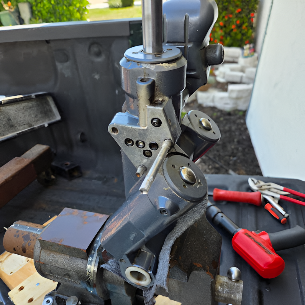A metal drill press machine is mounted in a vise, with tools in the background.